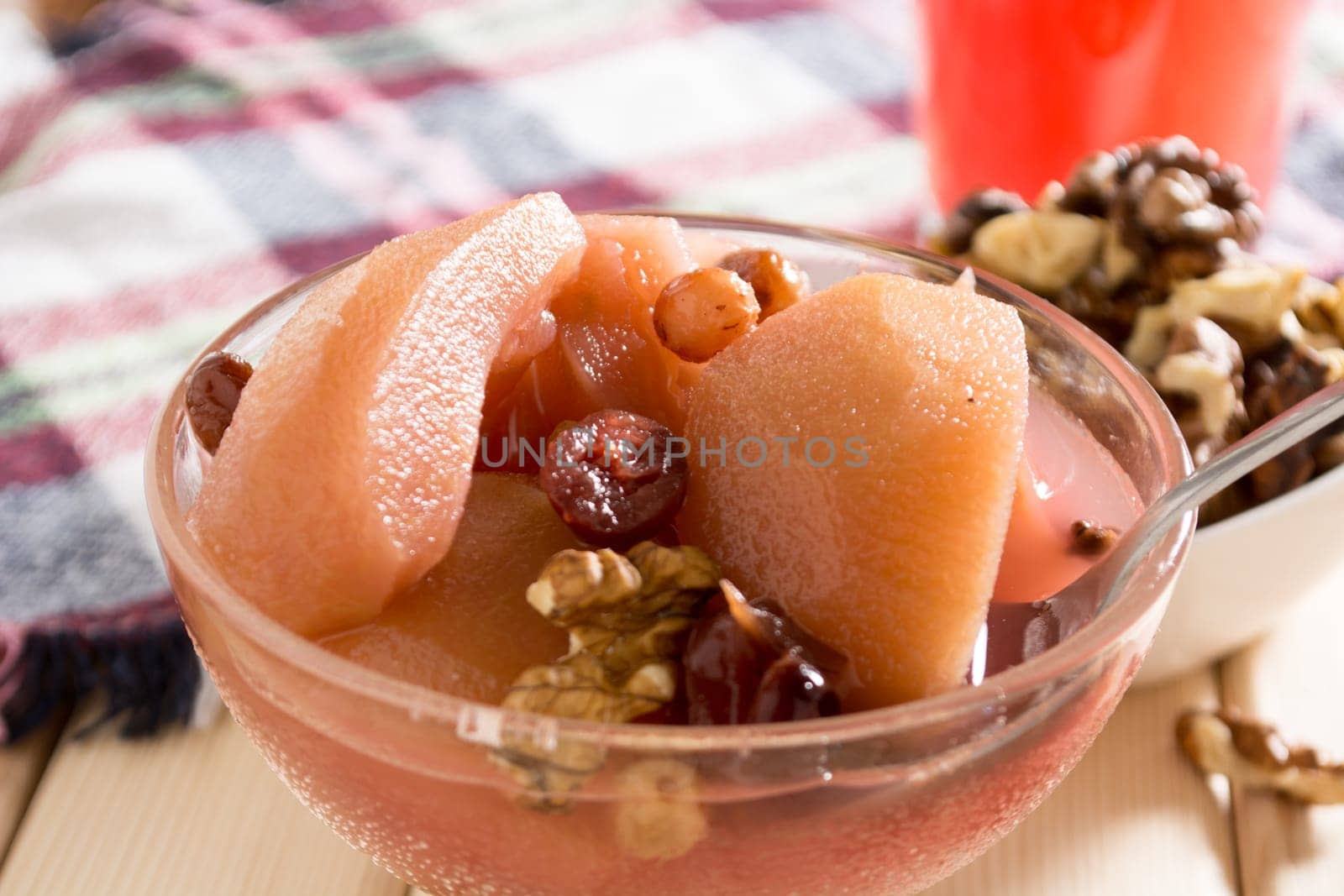 Apple compote with dried fruits in the cup on wooden table with decorative wallnuts