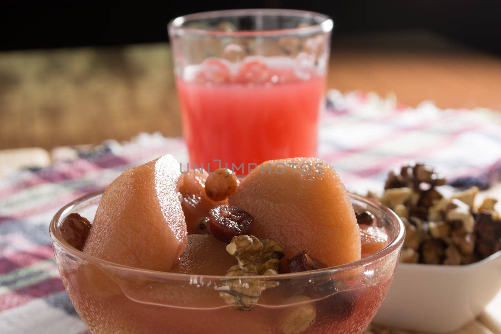 Apple compote with dried fruits in the cup on wooden table with decorative wallnuts