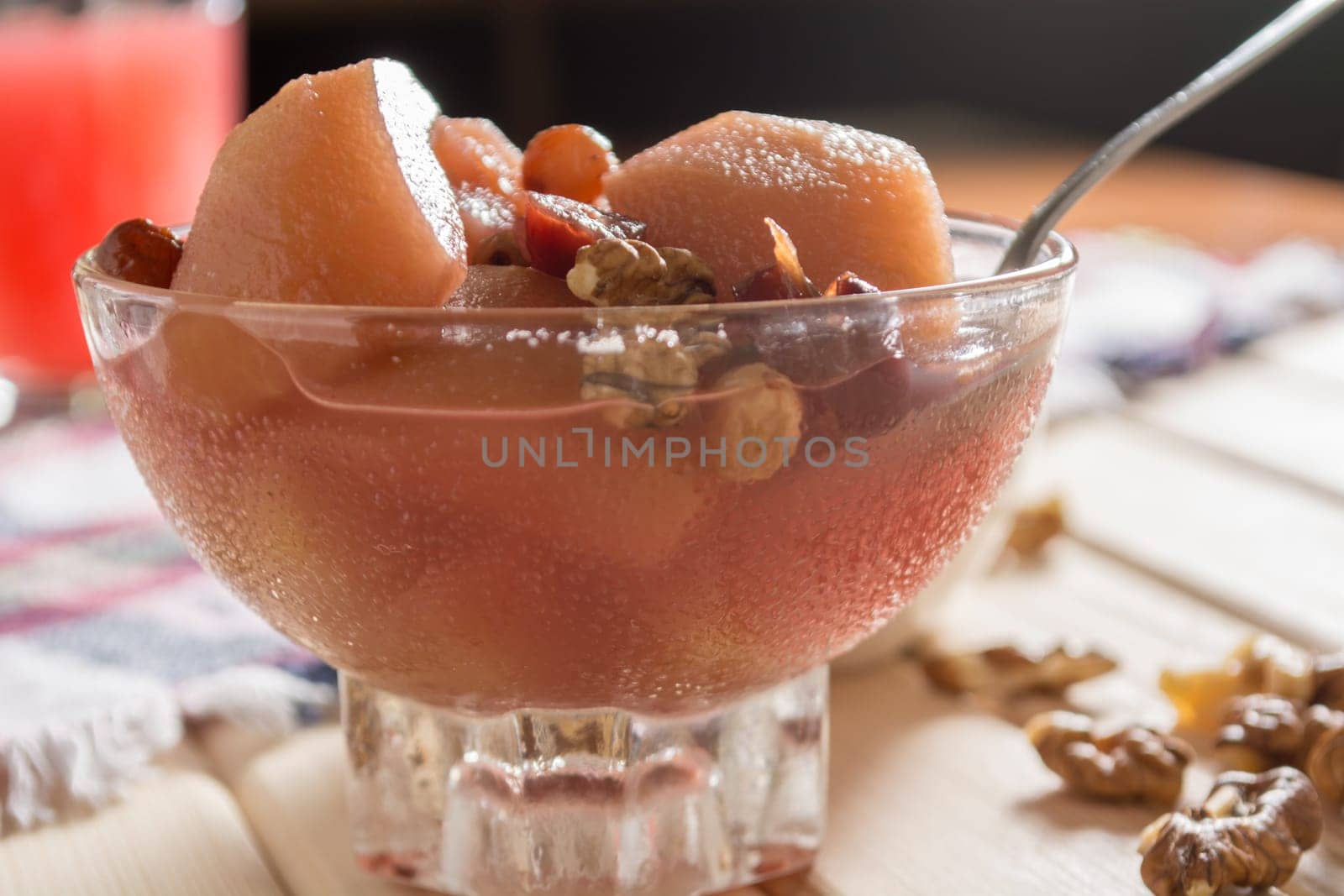 Apple compote with dried fruits in the cup on wooden table with decorative wallnuts