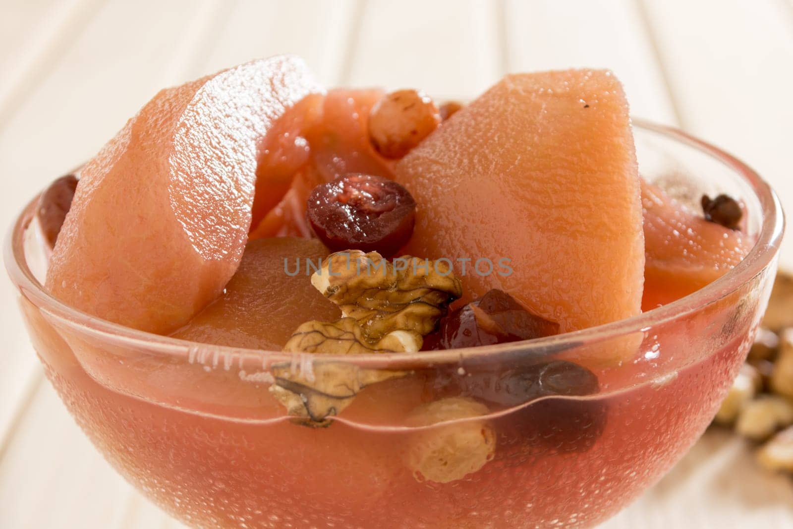 Apple compote with dried fruits in the cup on wooden table with decorative wallnuts