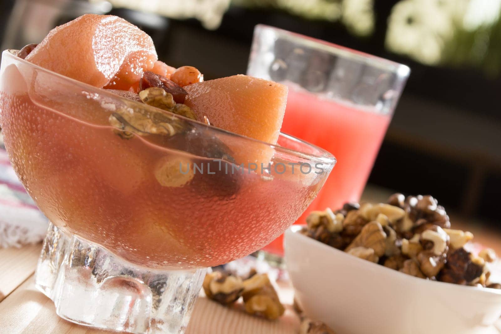Apple compote with dried fruits in the cup on wooden table with decorative wallnuts