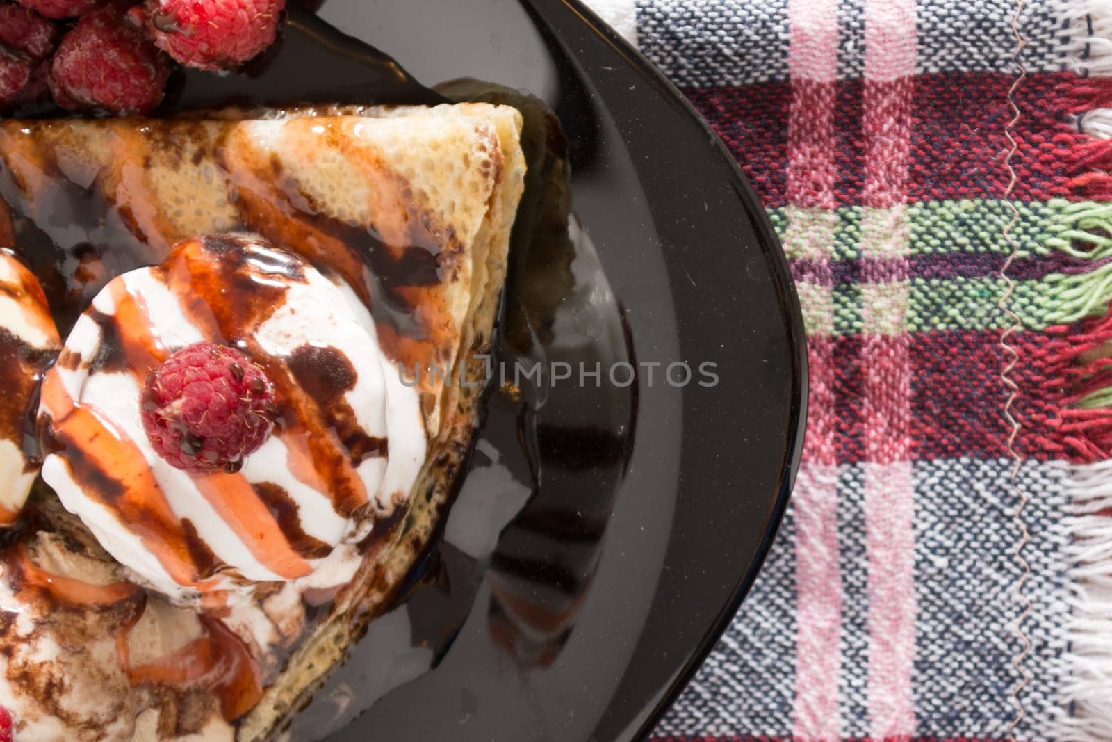 Fresh, golden pancakes with fruit and cream on a black plate with blurred background