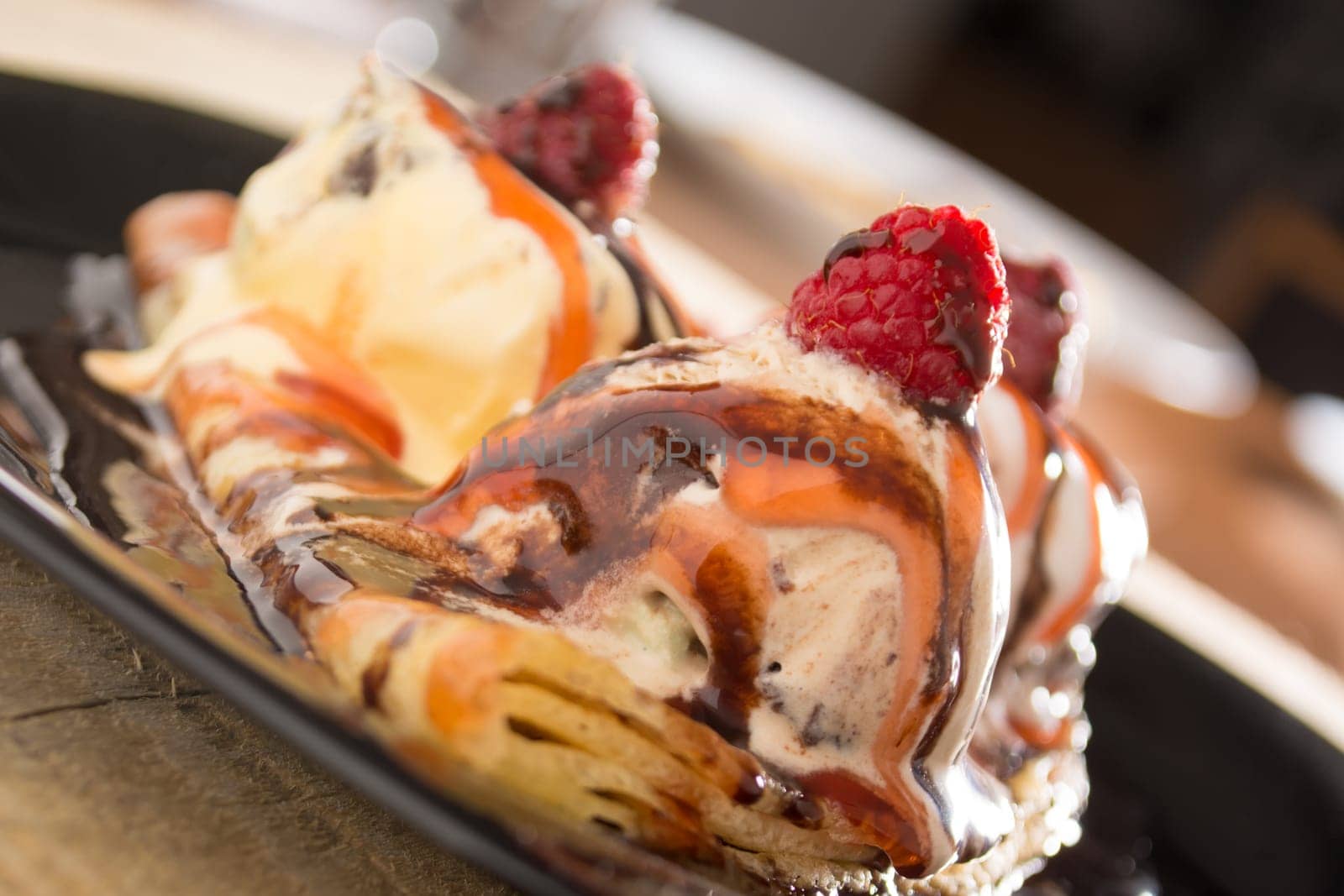 Fresh, golden pancakes with fruit and cream on a black plate with blurred background
