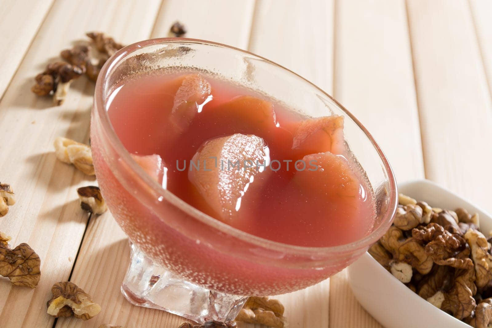 Apple compote with dried fruits in the cup on wooden table with decorative wallnuts