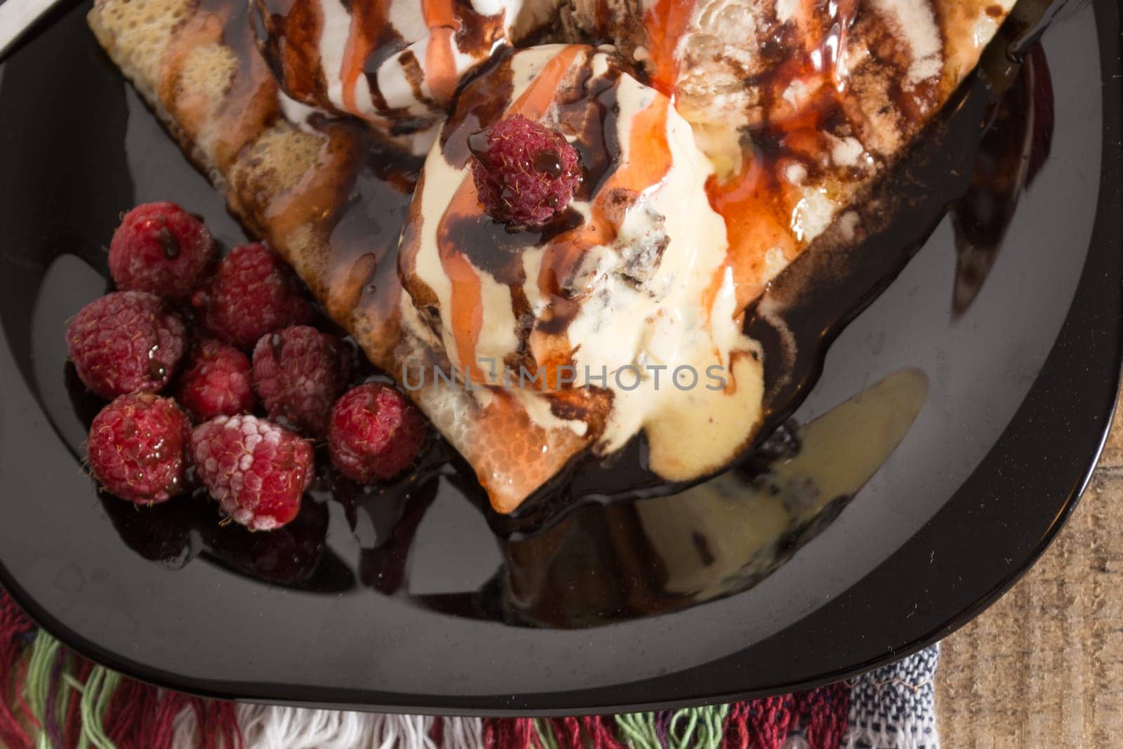 Fresh, golden pancakes with fruit and cream on a black plate with blurred background