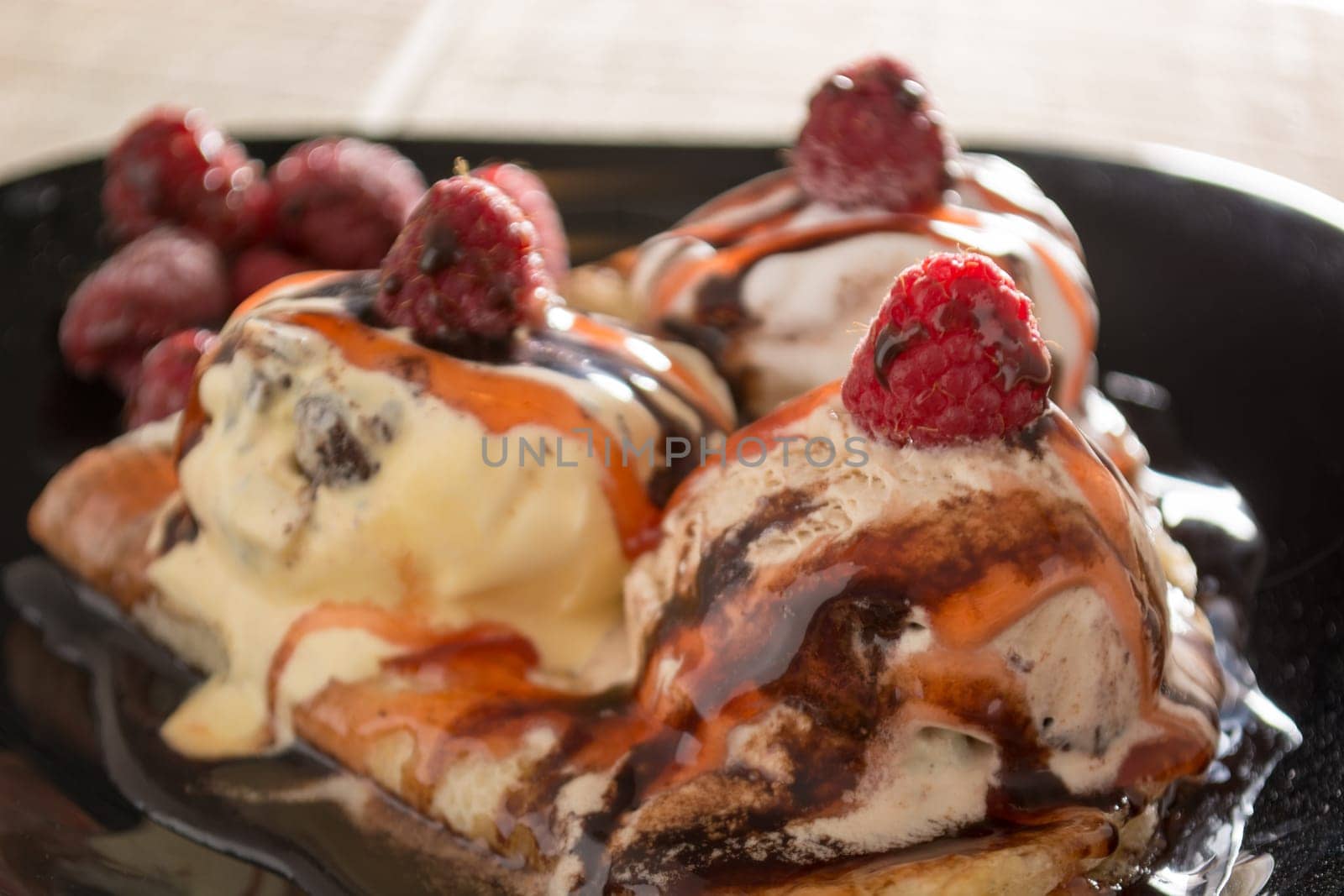 Fresh, golden pancakes with fruit and cream on a black plate with blurred background