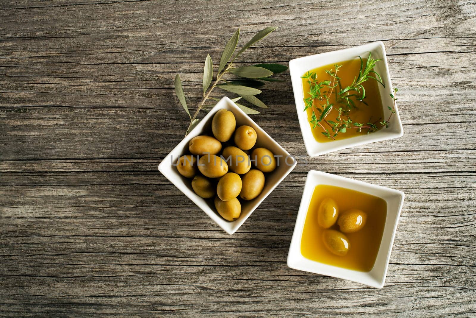 Olive oil with fresh herbs on wooden background.