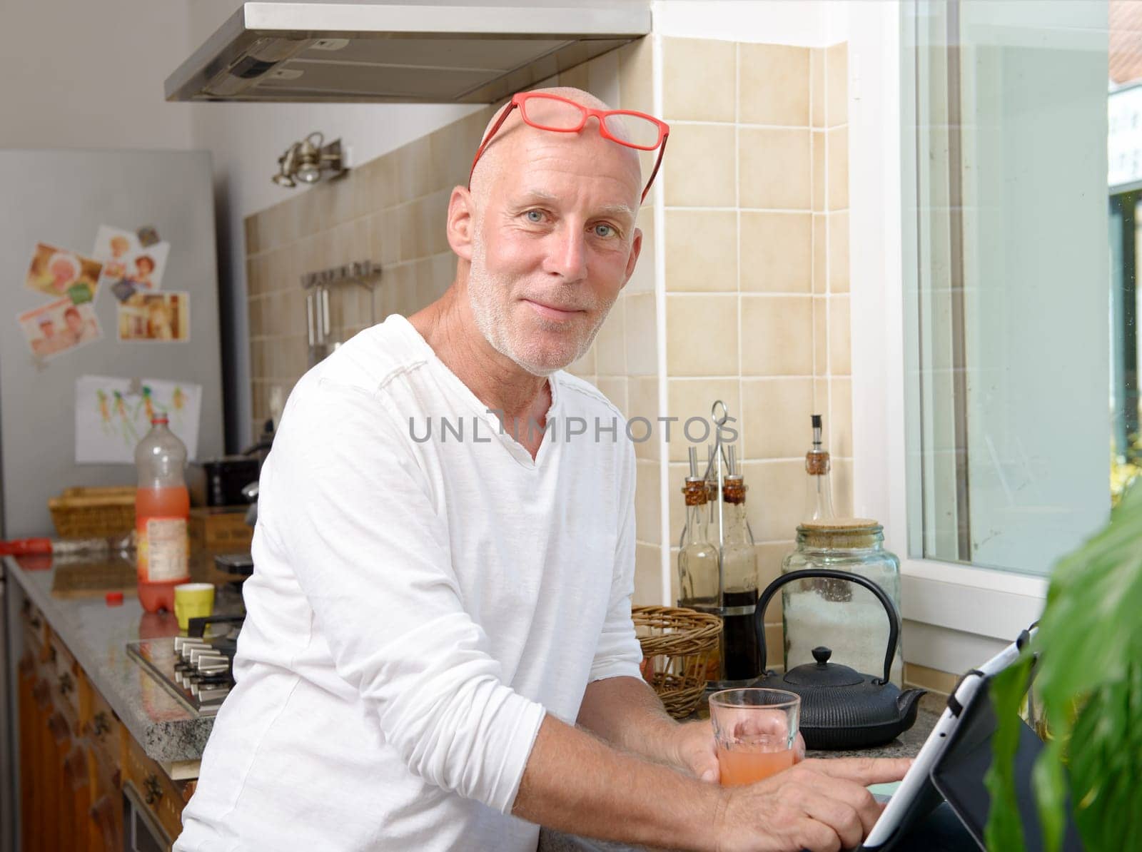 a senior man in kitchen using digital tablet and drink fruit juice