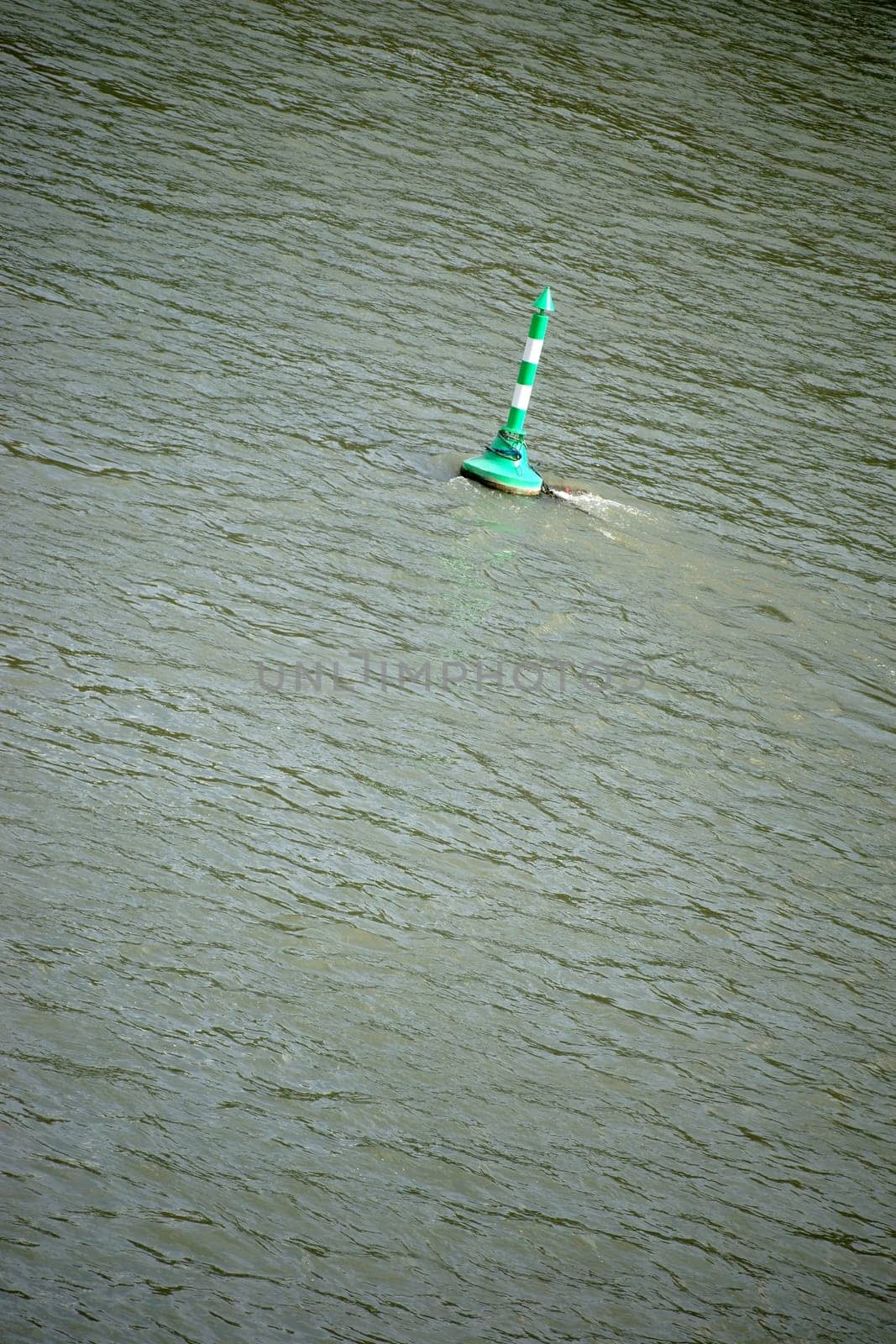 A green and white striped signal buoy on a river near an inland port.