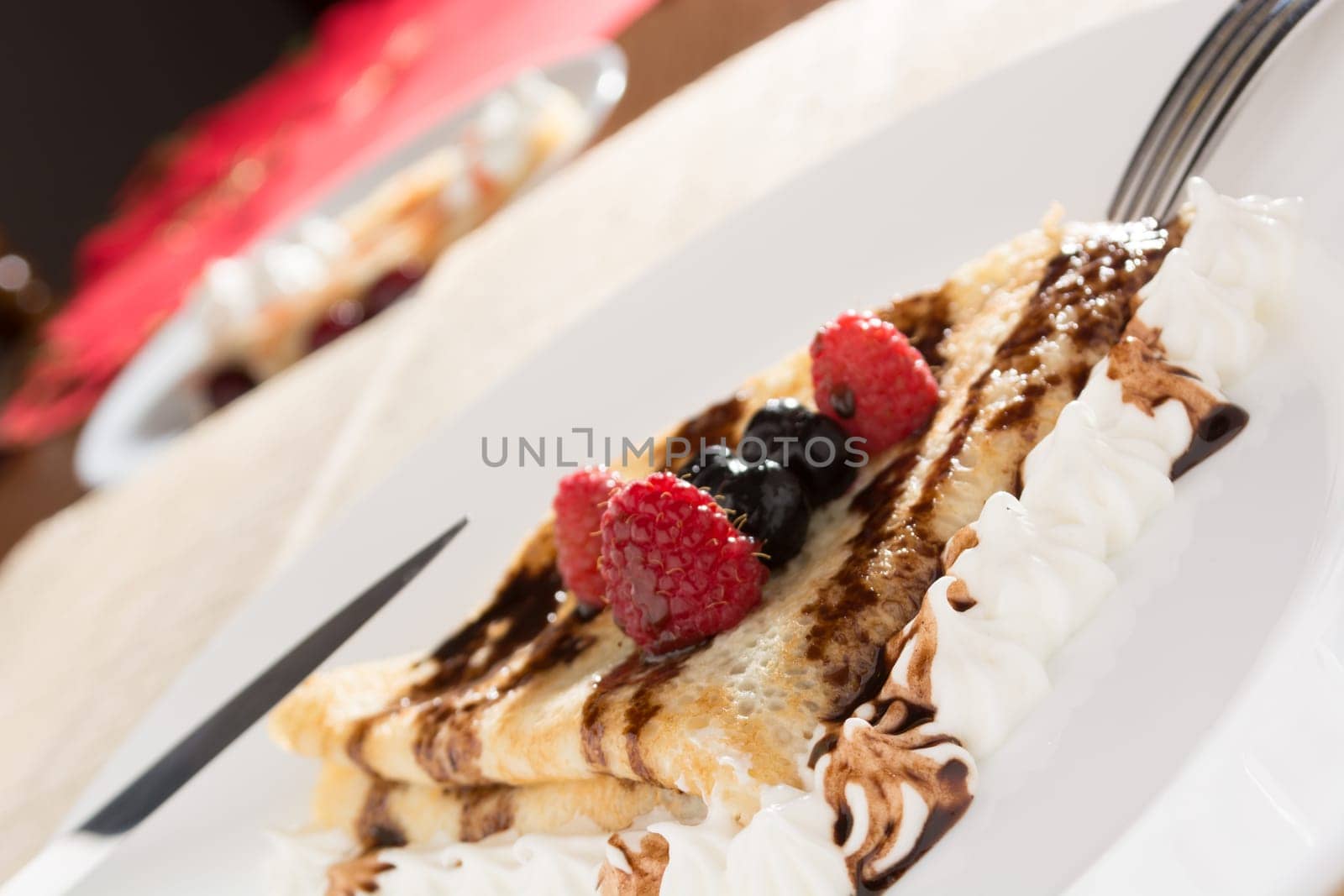 Fresh, golden pancakes with fruit and cream on a white plate with blurred background