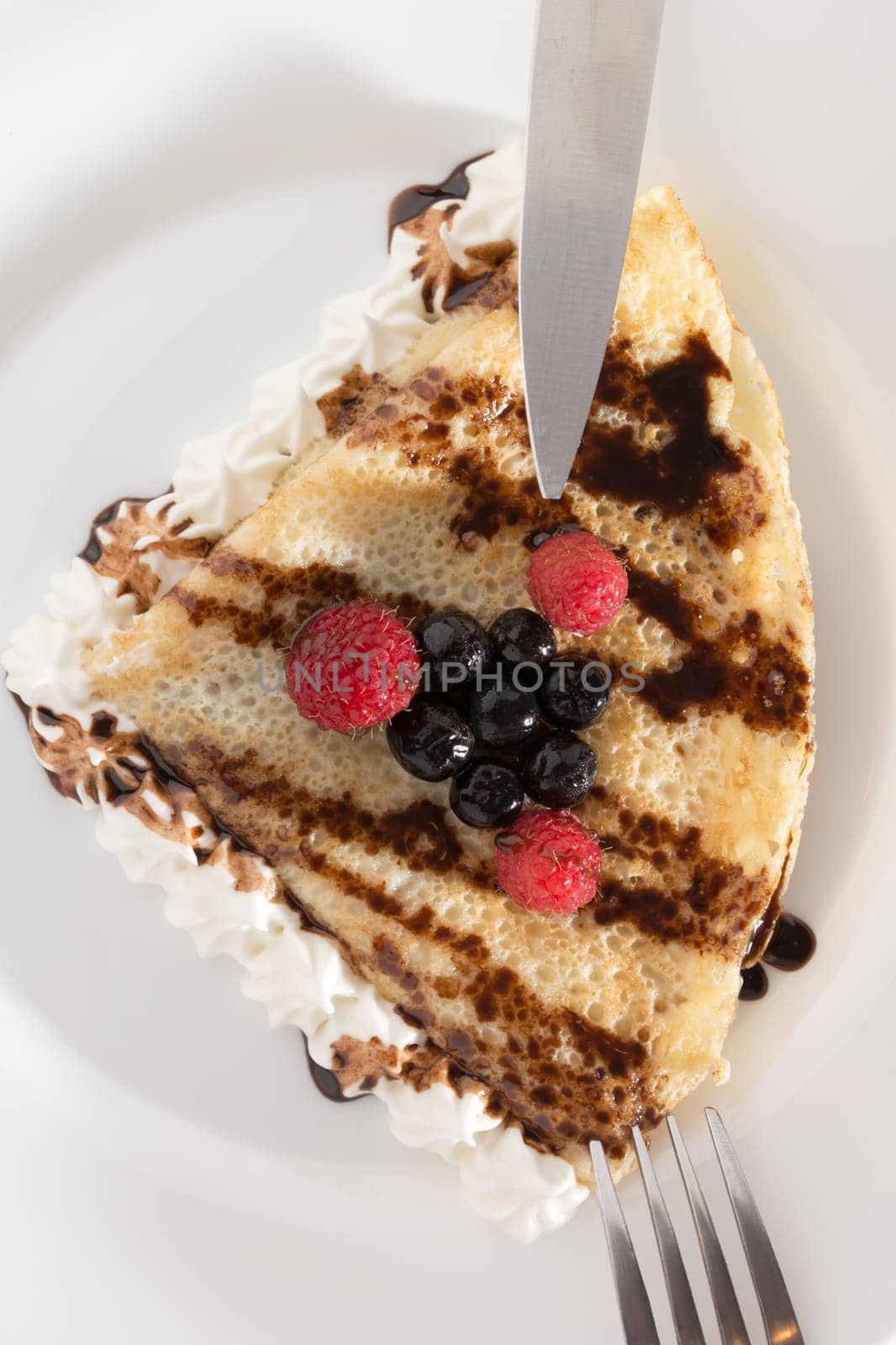 Fresh, golden pancakes with fruit and cream on a white plate with blurred background
