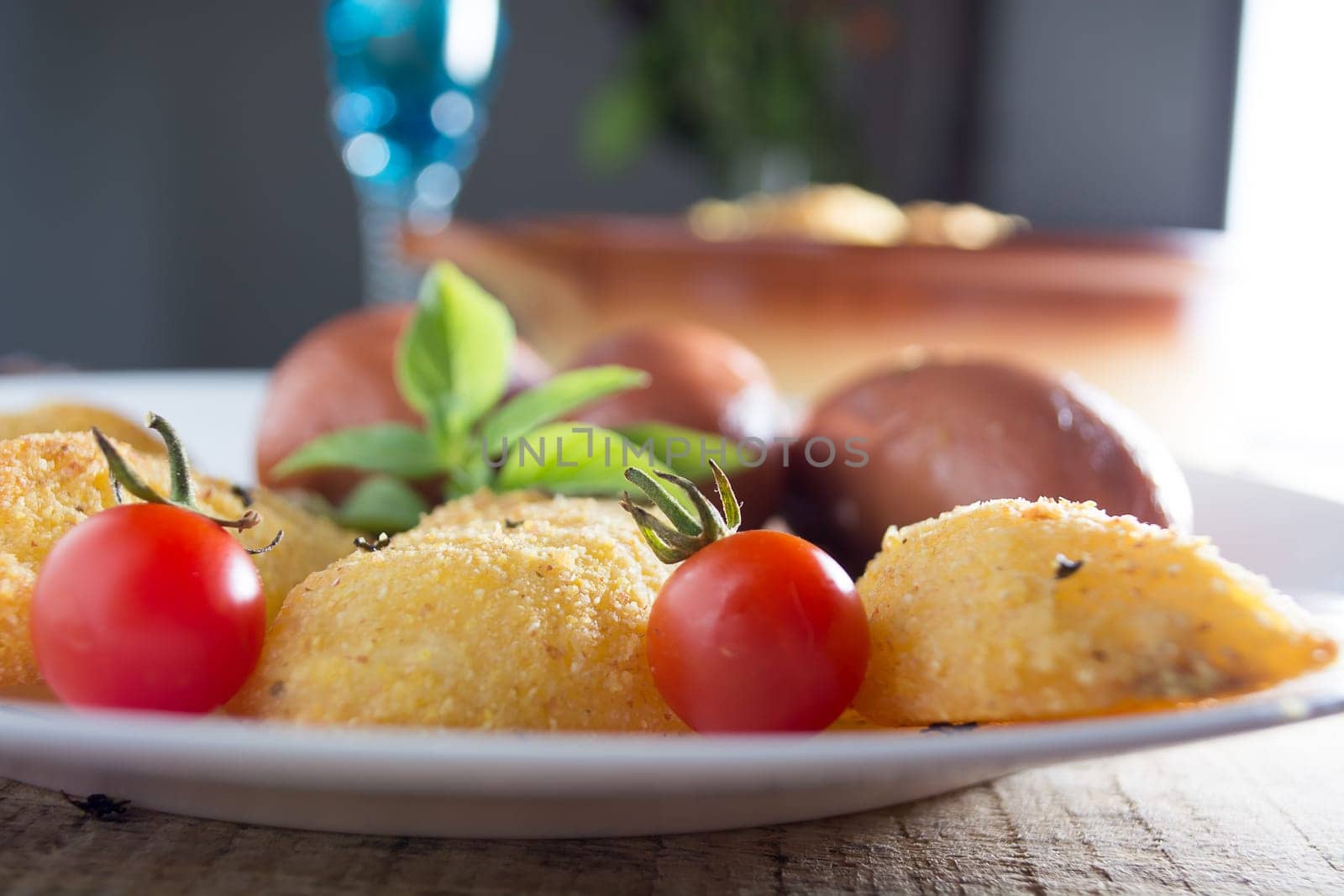 Pork sausages and breaded potatoes fried in a dish and decorated with cherry tomato placed on wooden table