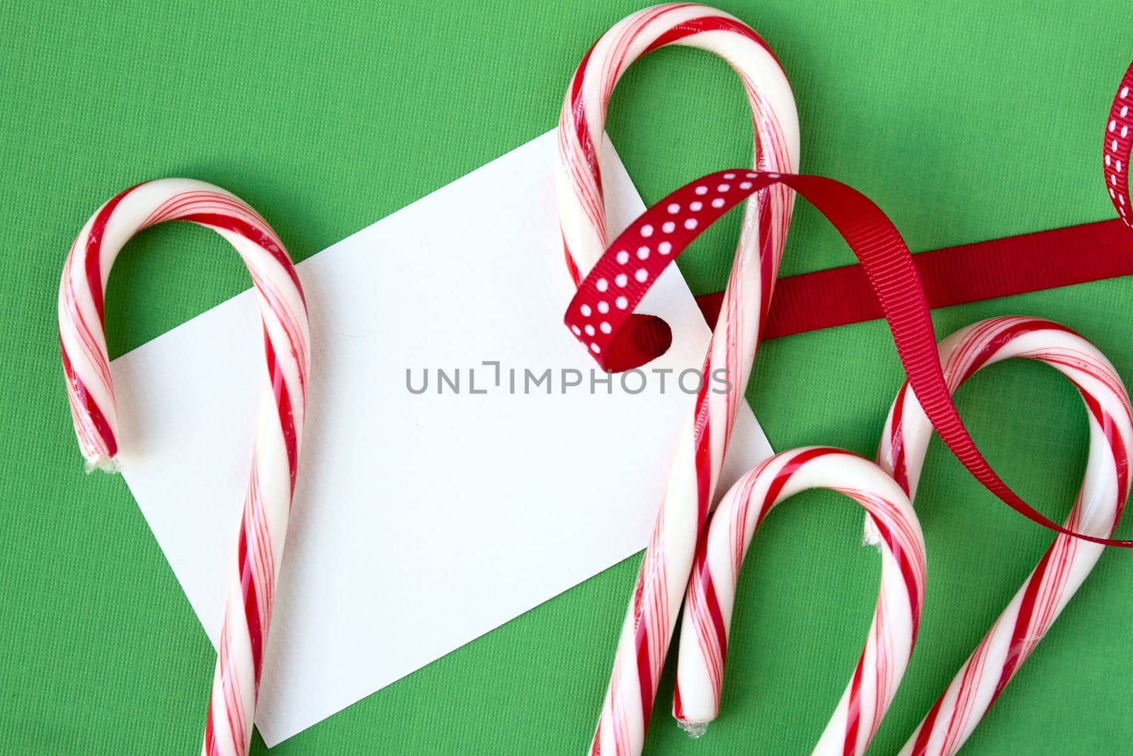 Candy canes and ribbon with copy space on gift tag, all on green background