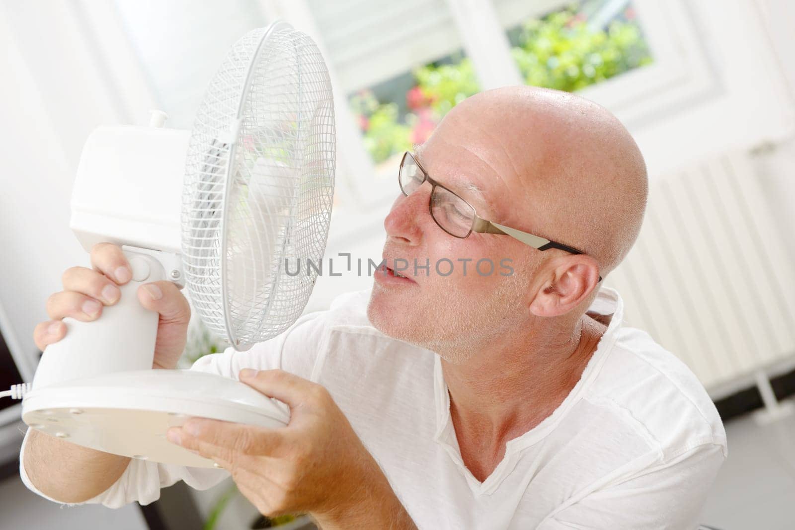 mature man refreshed with a fan in his home