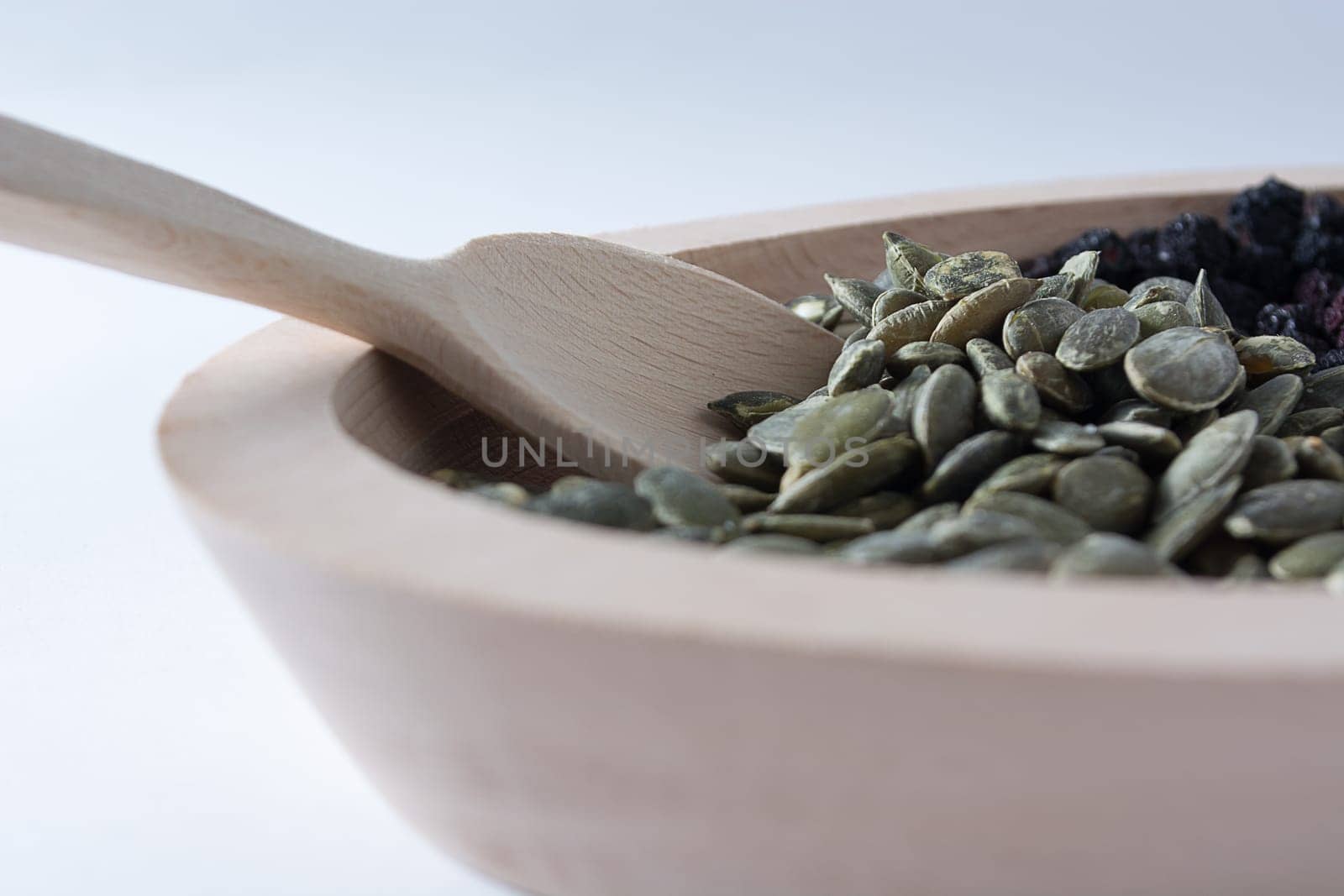 Aronia and pumpkin seeds in wooden bowl with wooden spoon isolated on white background