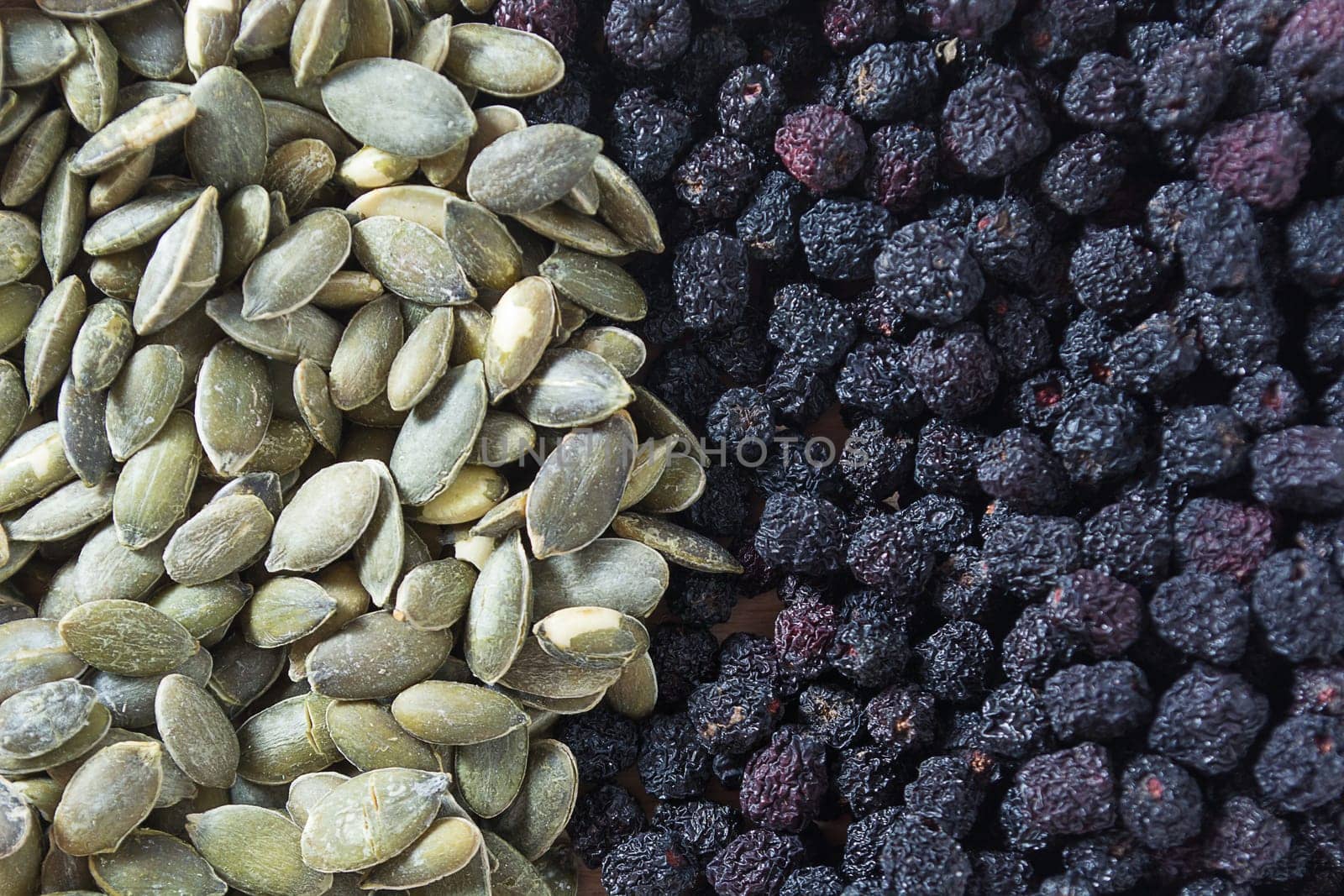 Aronia and pumpkin seeds in wooden bowl with wooden spoon isolated on white background