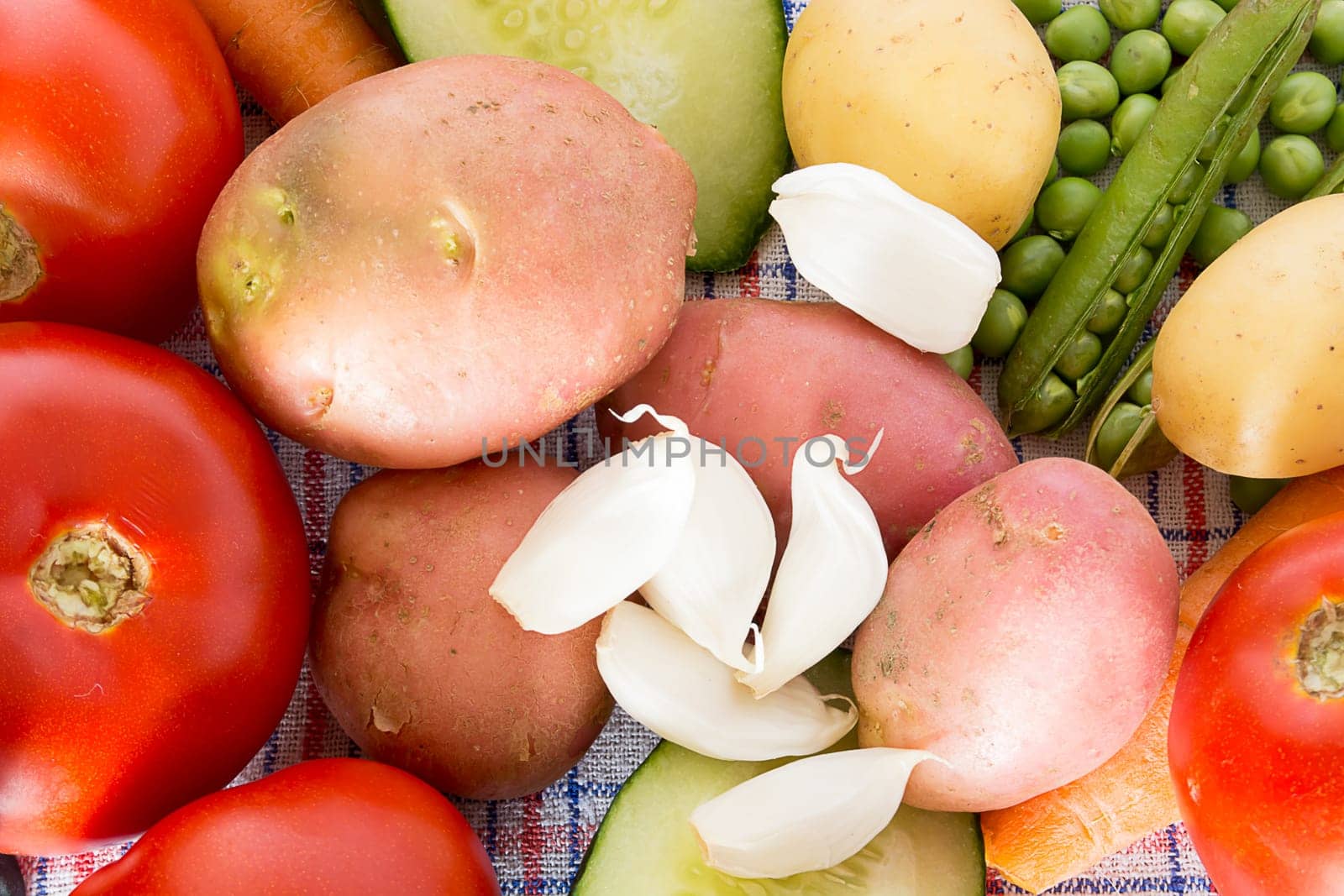 Various vegetable on a kitchen table. Carrots, potatoes, tomatoes, garlic, cucambers and green beans are visible
