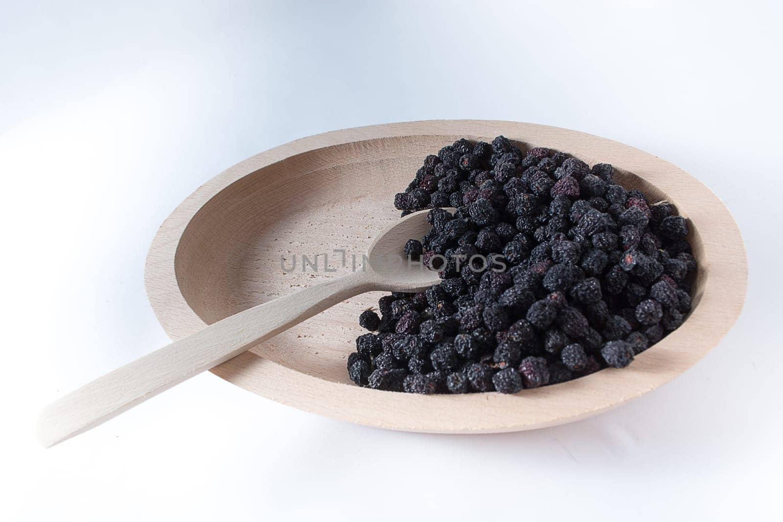 Aronia in wooden bowl with wooden spoon isolated on white background