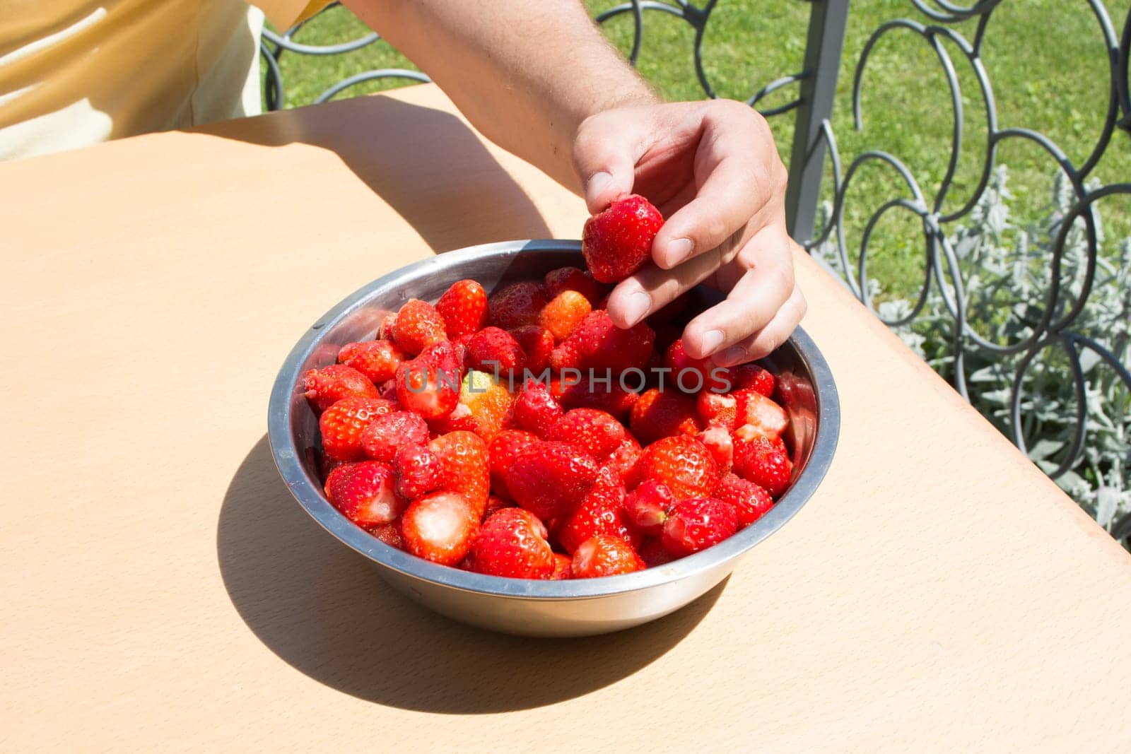 Hand picking strawberries from metal bowl