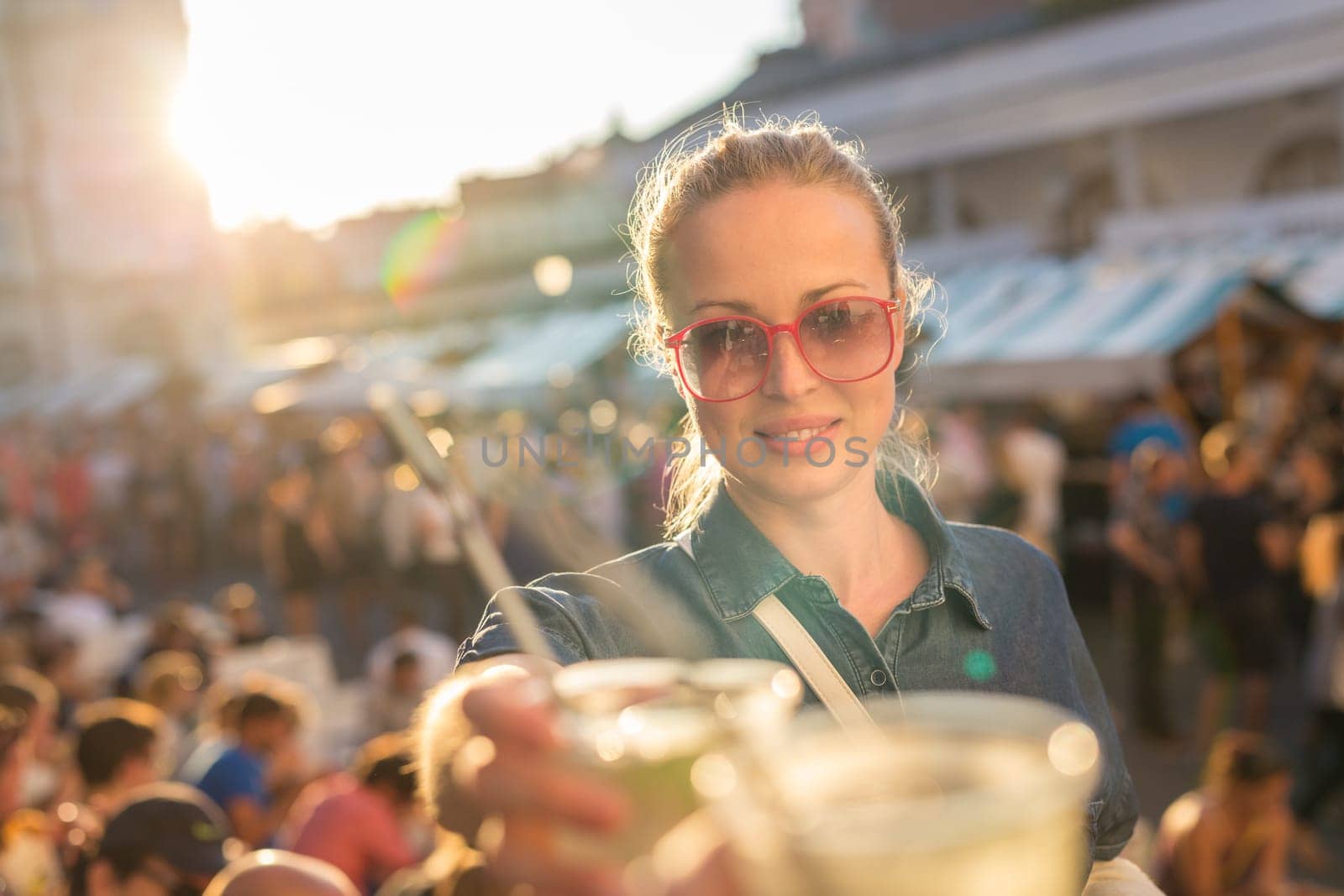 Beautiful young girl toasting outdoors on Open kitchen street food festival in Ljubljana, Slovenia. Popular summer urban tourist event in capital.