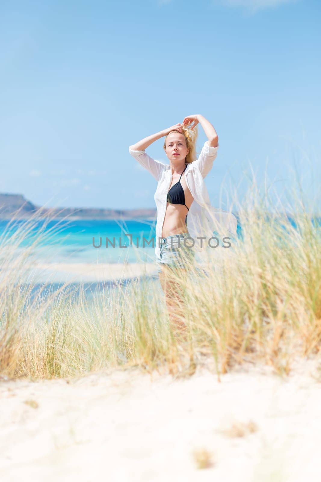 Relaxed woman wearing unpinned white shirt and black bikin, enjoying sun, freedom and life an a beautiful beach. Young lady feeling free, relaxed and happy. Concept of health well being.