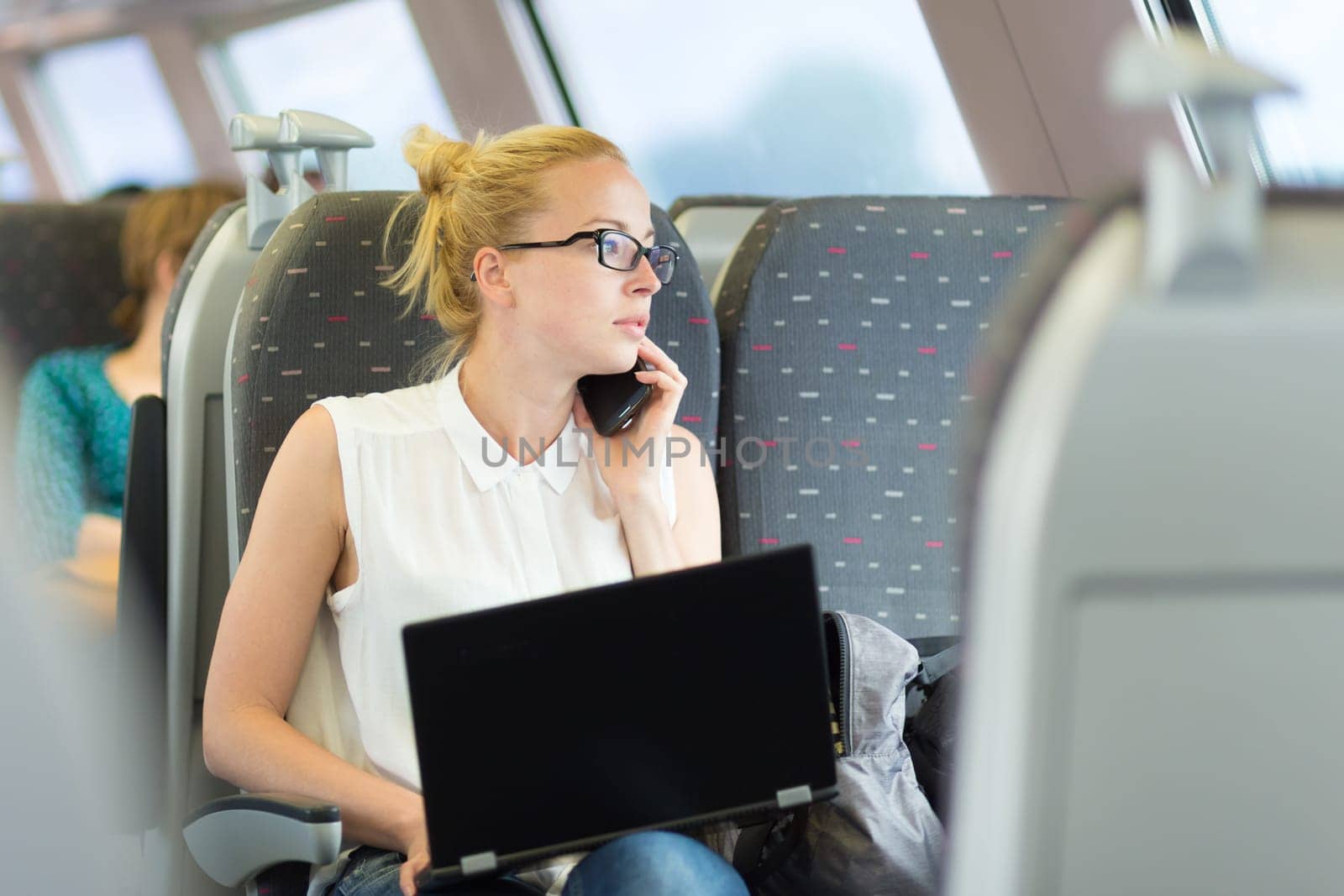 Businesswoman talking on cellphone and working on laptop while traveling by train. Business travel concept.