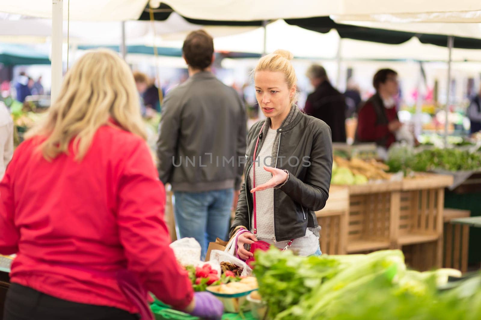 Woman buying fruits and vegetables at local food market. Market stall with variety of organic vegetable.