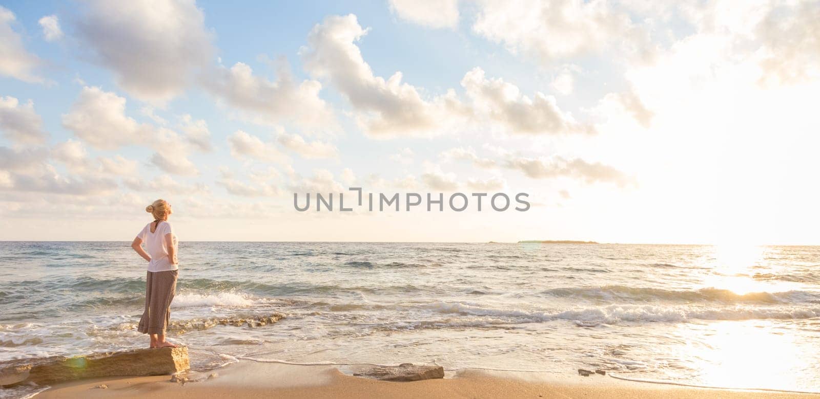 Relaxed woman enjoying sun, freedom and life an beautiful beach in sunset. Young lady feeling free, relaxed and happy. Concept of vacations, freedom, happiness, enjoyment and well being.