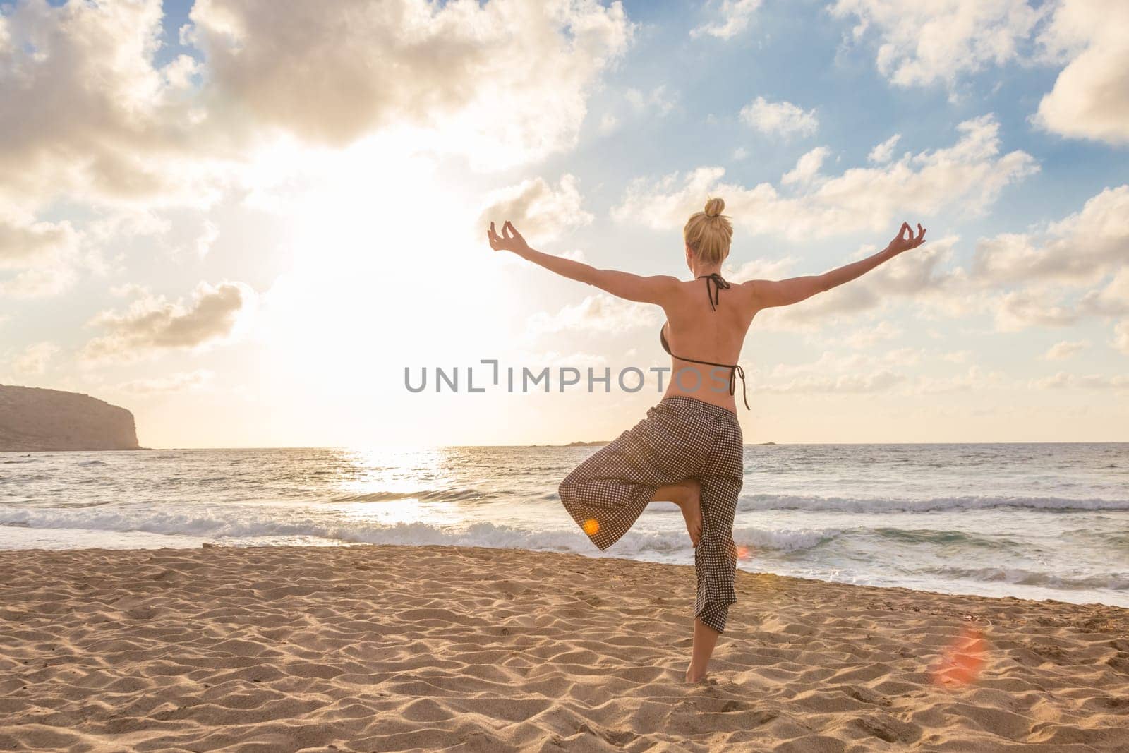 Active young woman practicing yoga on beach at sunset.