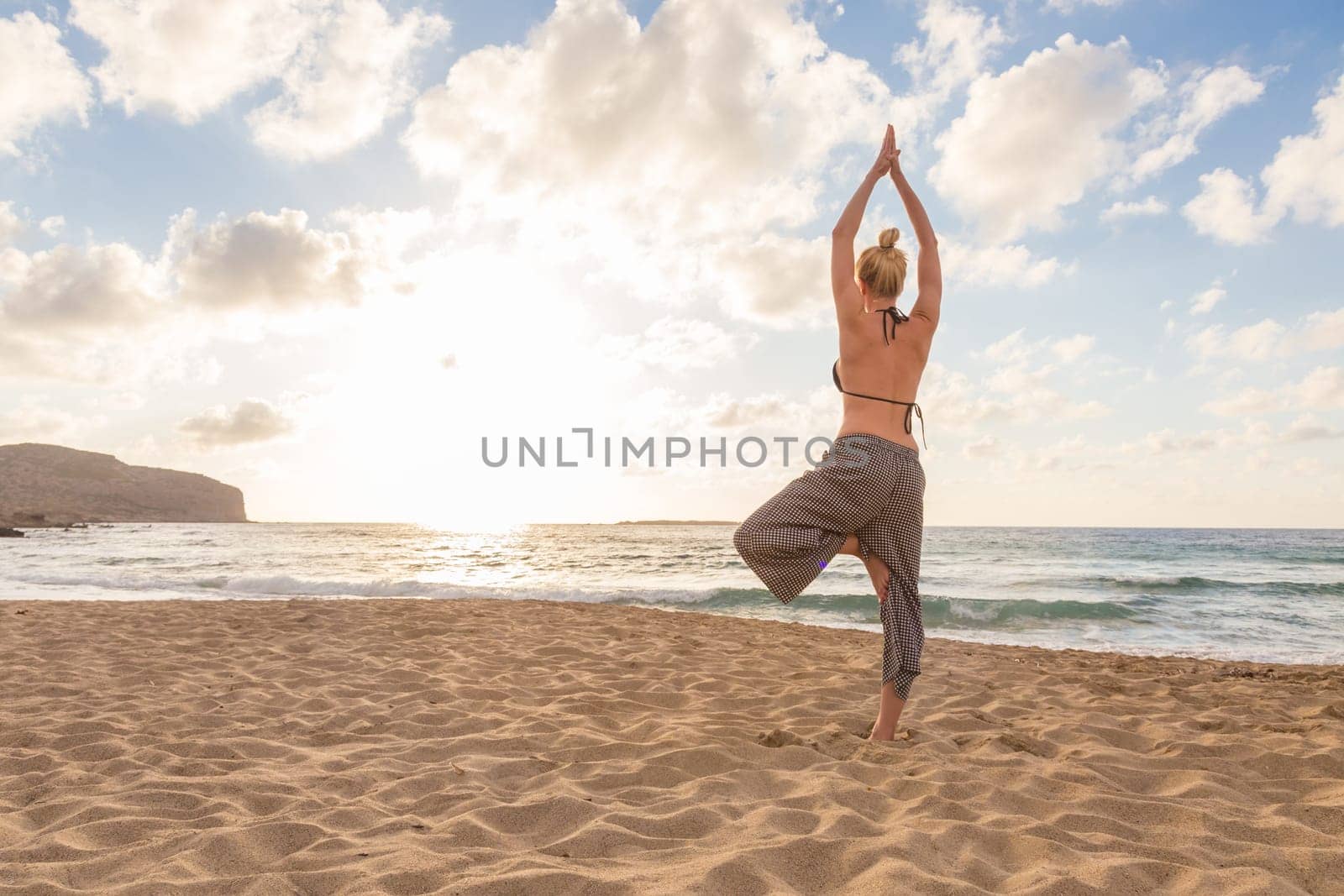 Active young woman practicing yoga on beach at sunset.
