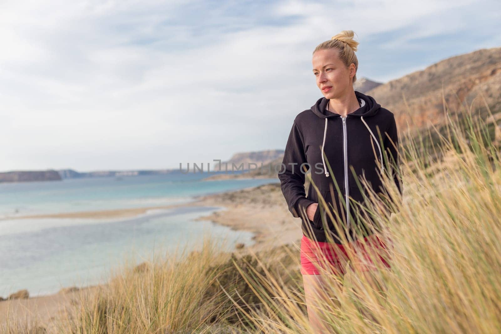 Relaxed woman in dark hoodie walking on serene Balos beach, Greece, enjoying beautiful nature and nice views.