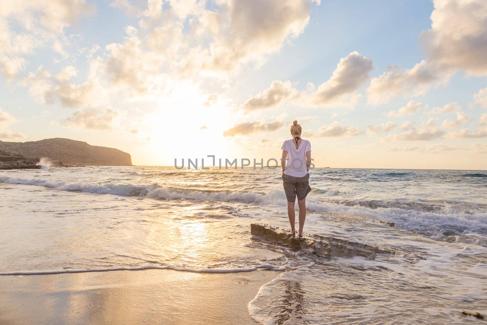 Relaxed woman enjoying sun, freedom and life an beautiful beach in sunset. Young lady feeling free, relaxed and happy. Concept of vacations, freedom, happiness, enjoyment and well being.