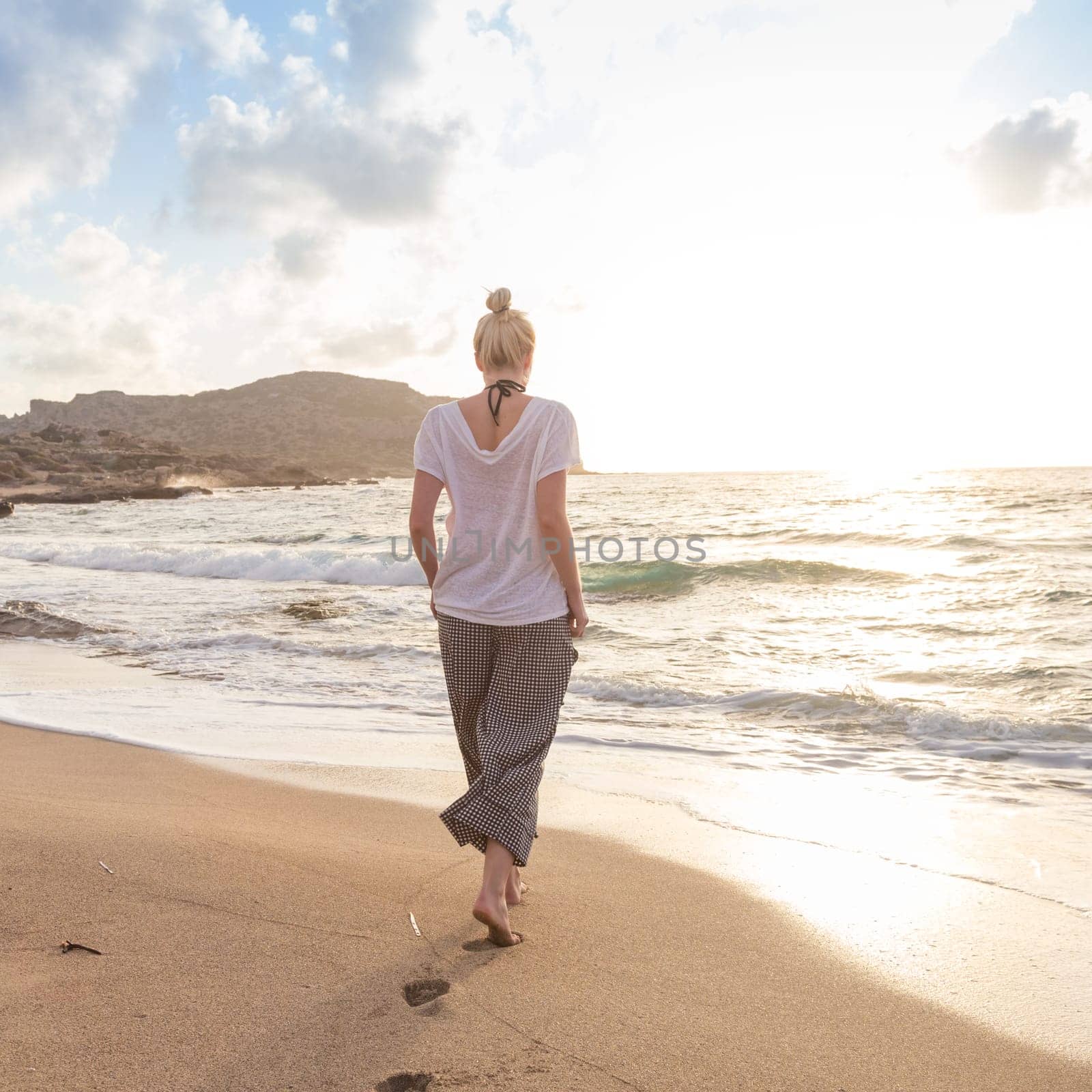 Woman walking on sand beach at golden hour. Seashore sunset walk.