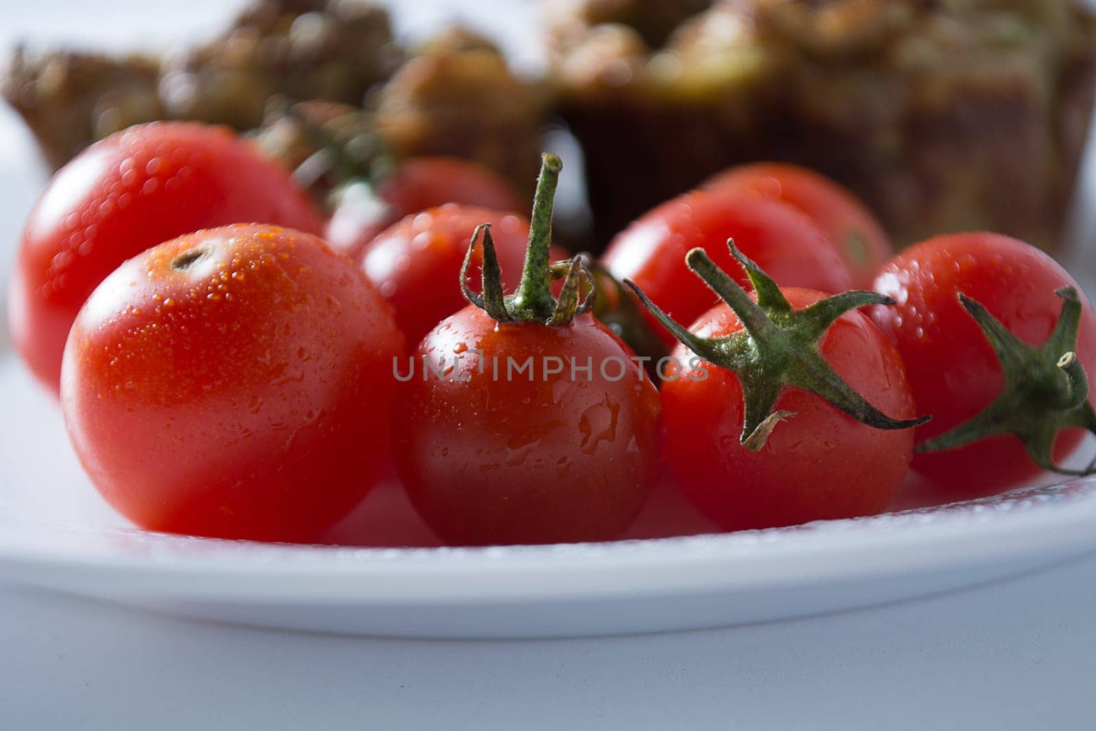 Ripe and red cherry tomatoes with zucchini muffins in white plate isolated on white background