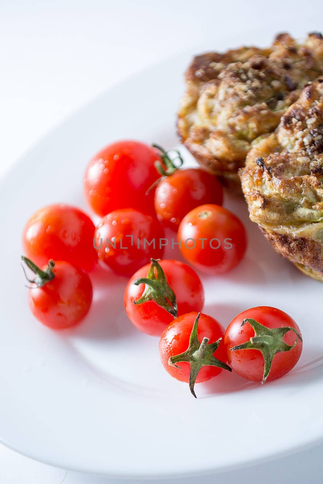 Ripe and red cherry tomatoes with zucchini muffins in white plate isolated on white background