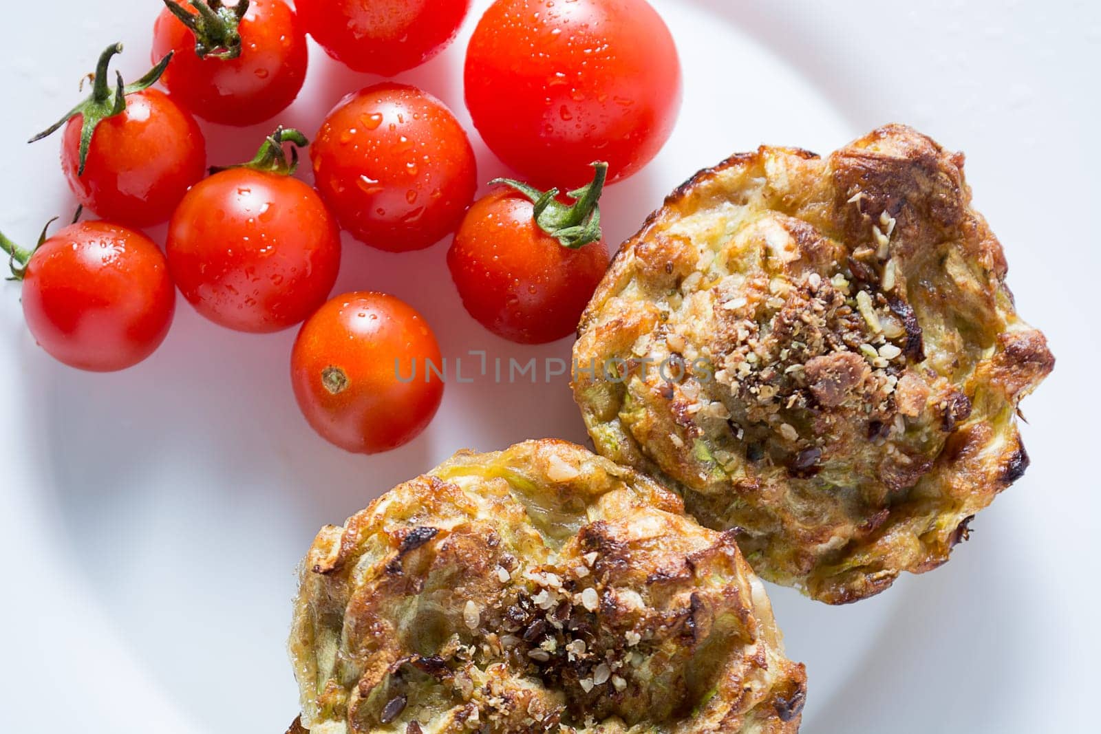 Ripe and red cherry tomatoes with zucchini muffins in white plate isolated on white background