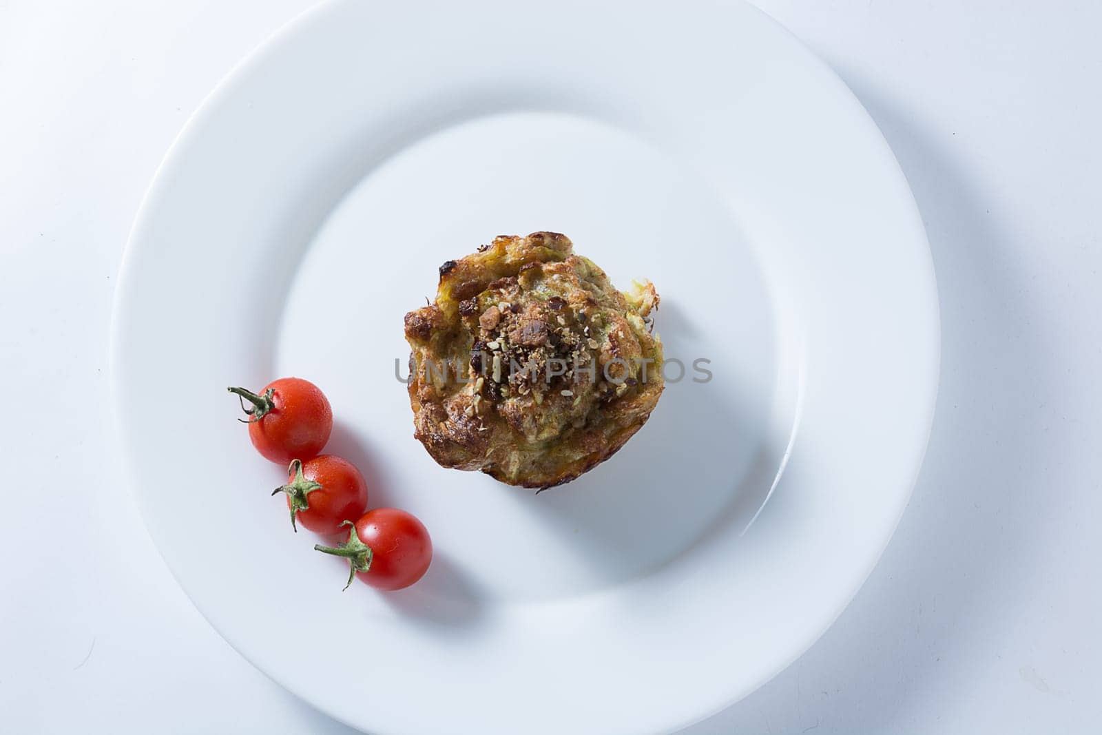 Ripe and red cherry tomatoes with zucchini muffins in white plate isolated on white background