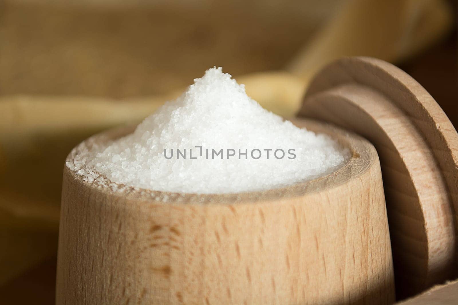 Close up of small wooden cup full of salt sitting on the kitchen table. Other kitchen wares blurred in the background