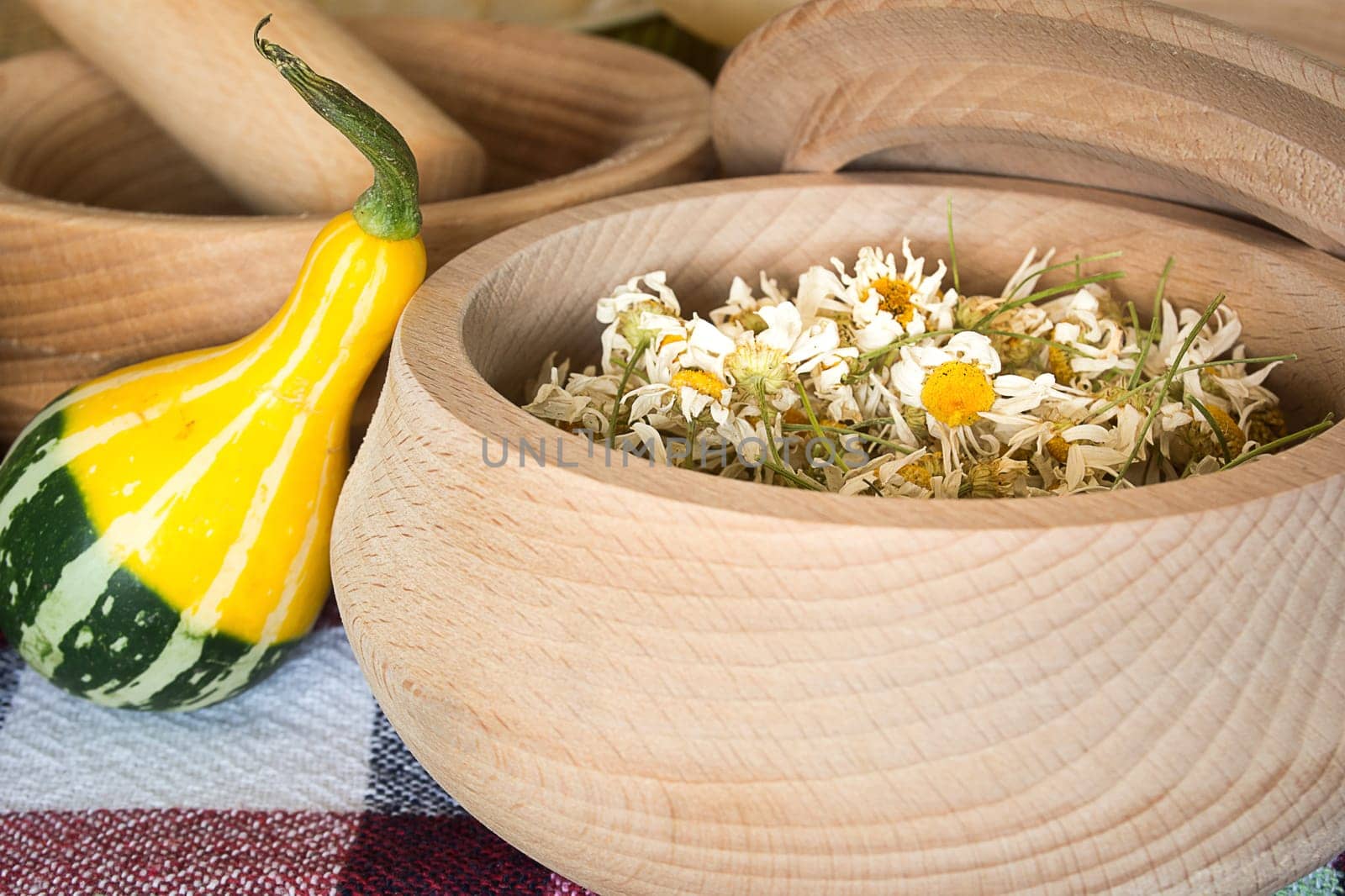 Dried chamomile flowers in wooden bowl placed on rustic table with decorative pumpkin