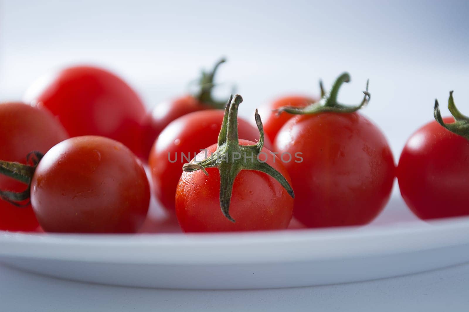 Ripe and red cherry tomatoes in white plate isolated on white background