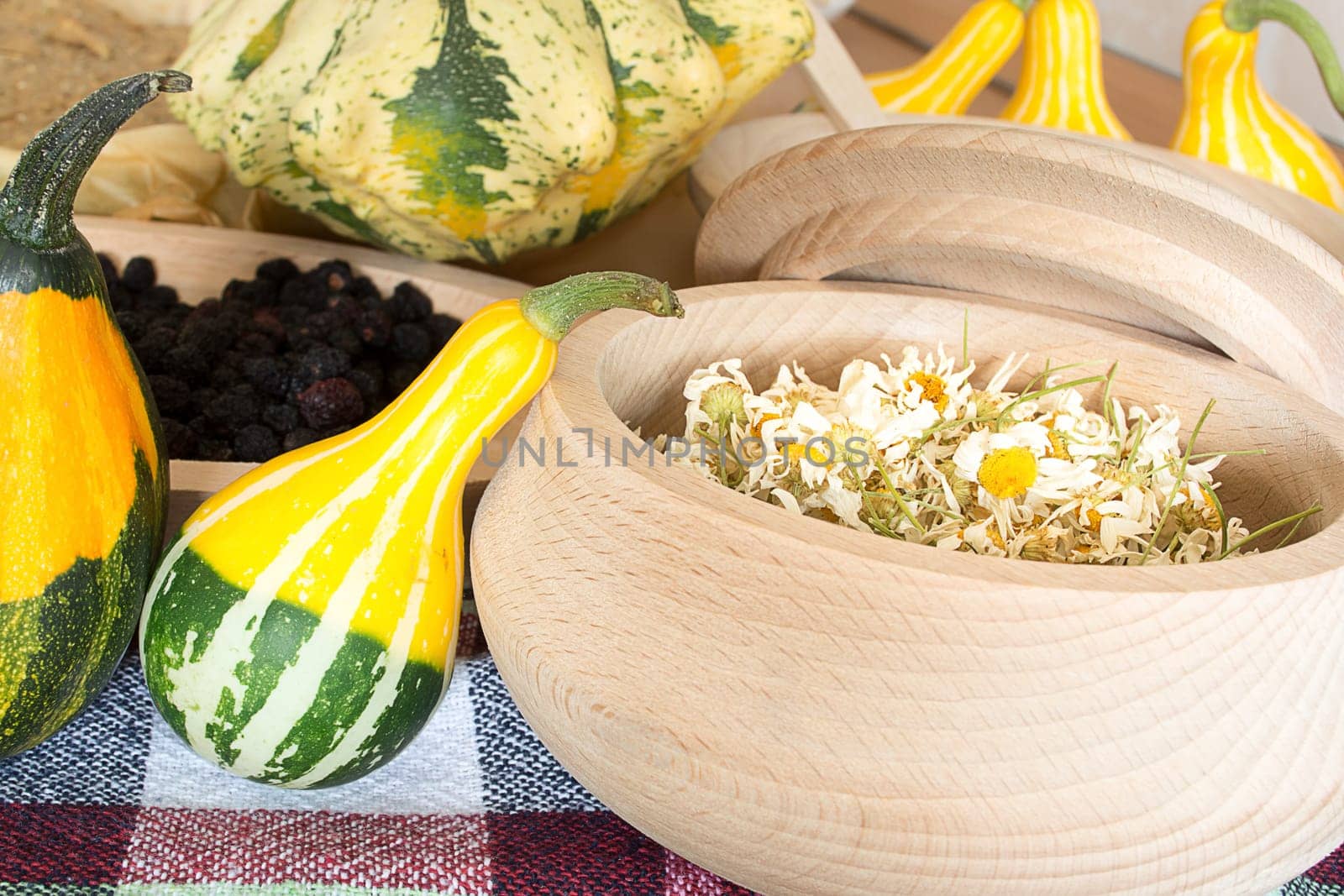 Dried chamomile flowers in wooden bowl placed on rustic table with decorative pumpkin