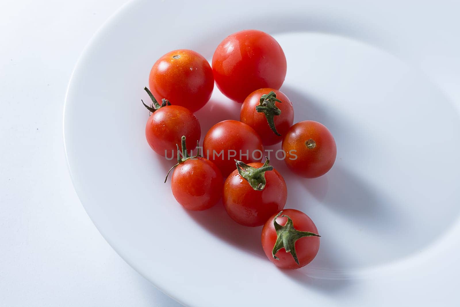 Ripe and red cherry tomatoes in white plate isolated on white background