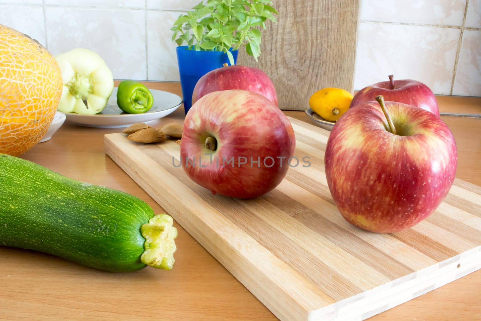 Group of apples on wooden plate, ready to be sliced and eaten. Various vegetables around the plate