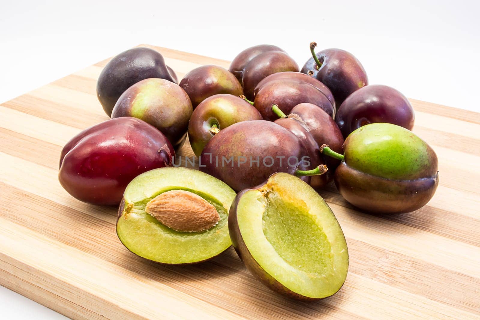 Juicy plum cuted in half on wooden board. Group of plums visible. Isolated on white background
