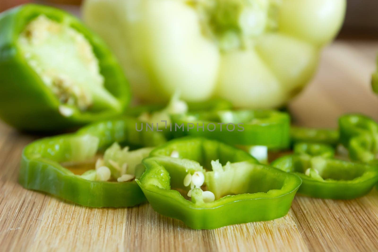 Sliced green pepper on wooden plate. Other vegetable is visible in the background