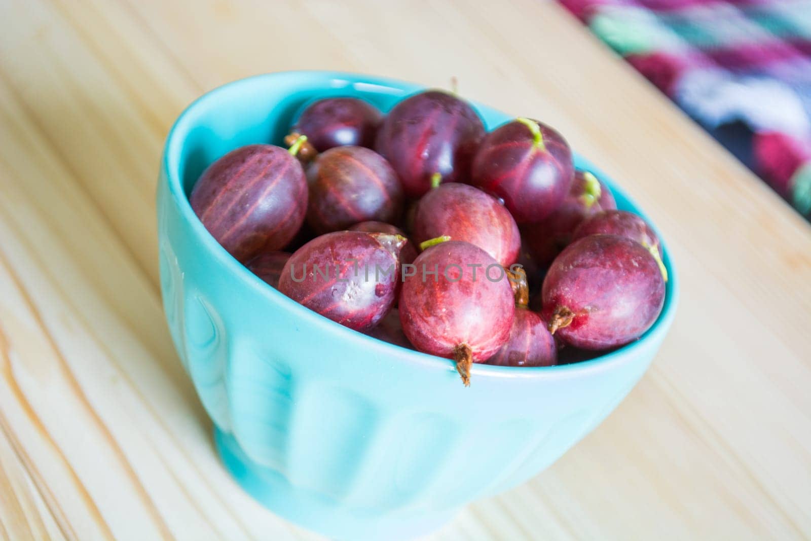 Gooseberry in blue ceramic bowl on the kitchen table. Blurred background
