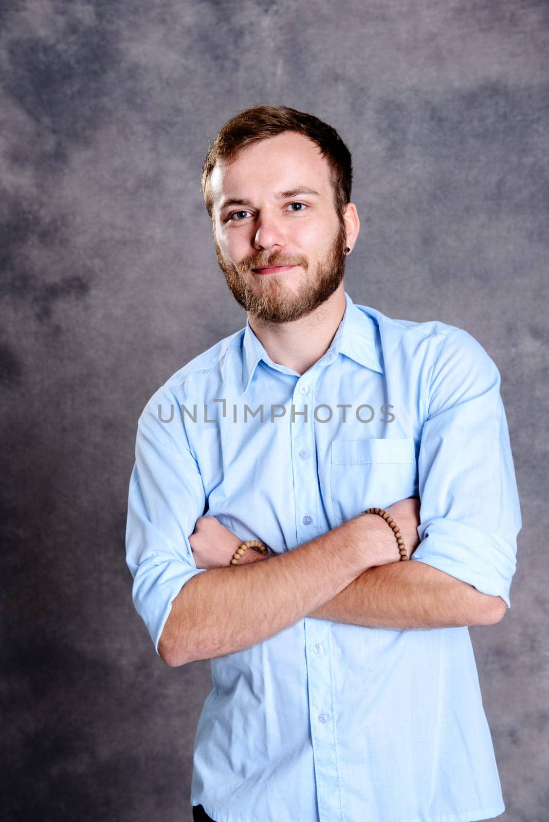 young bearded man with crossed arms in front of gray background