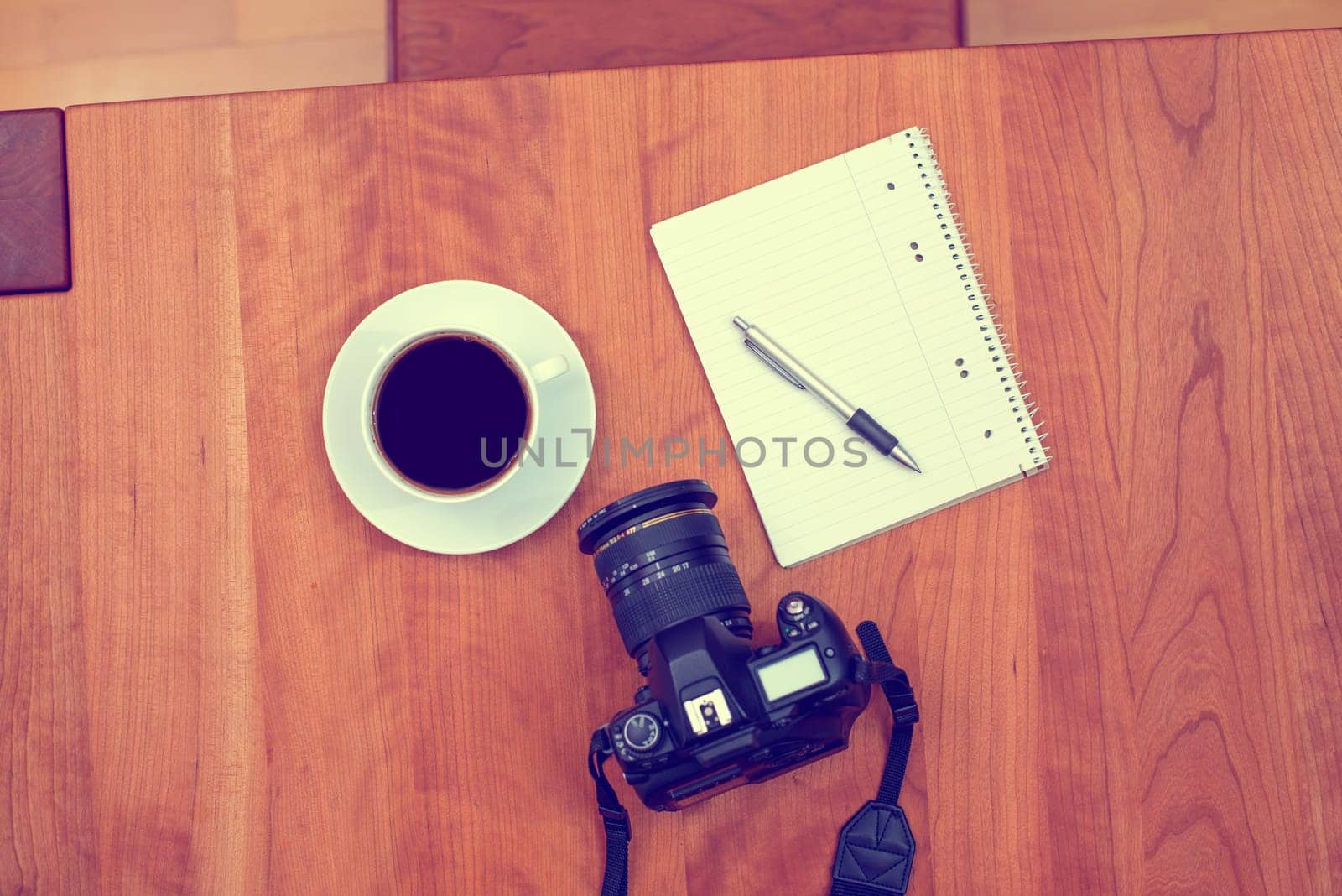camera, notepad with pen and coffee on wooden table from above