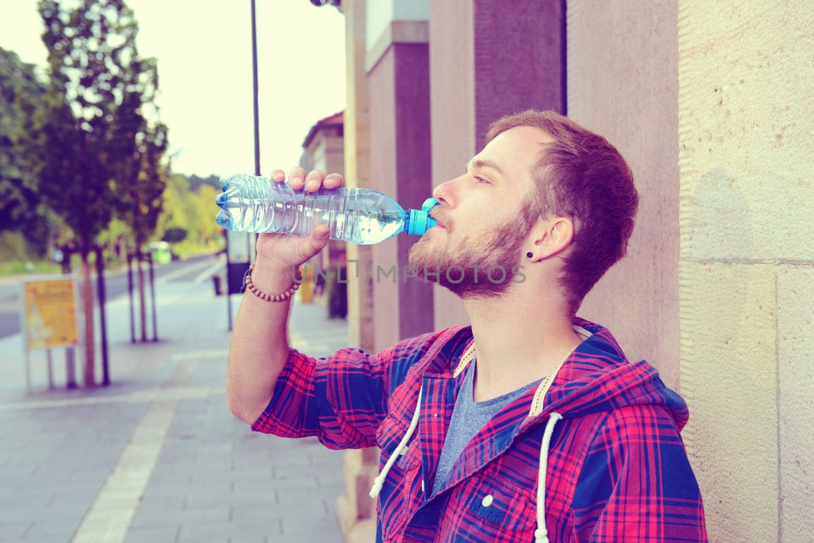 young bearded man with water bottle in checkered shirt in front of city- background