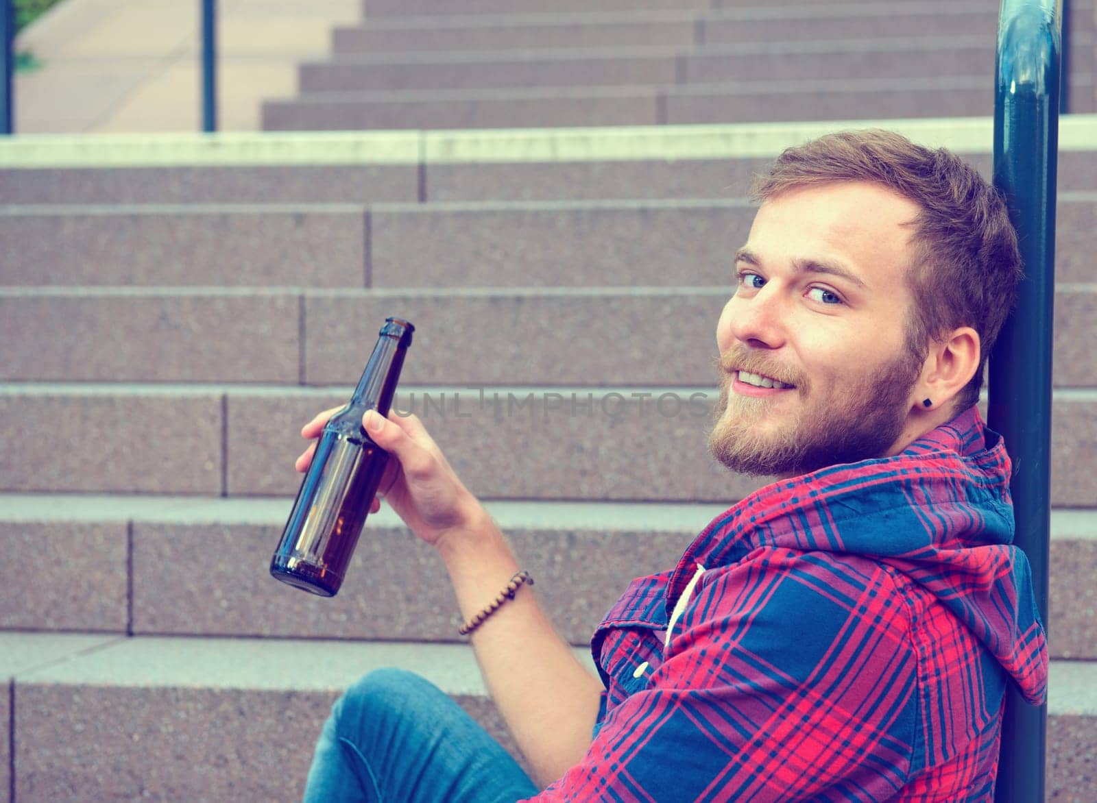 young bearded man with bottle in checkered shirt sitting on stairs